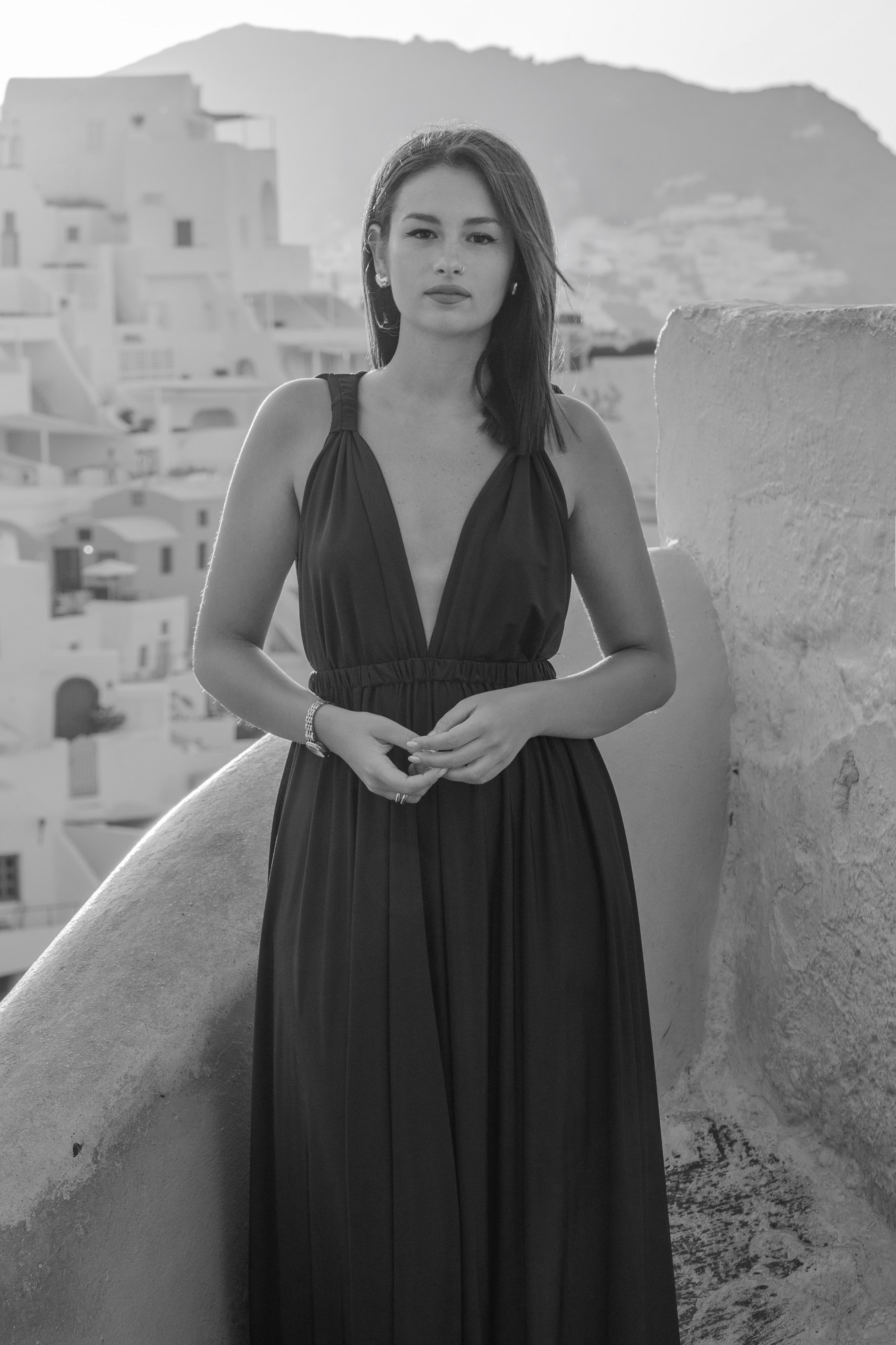 A woman in a black dress standing outdoors with white buildings and a mountain in the background, in black and white.