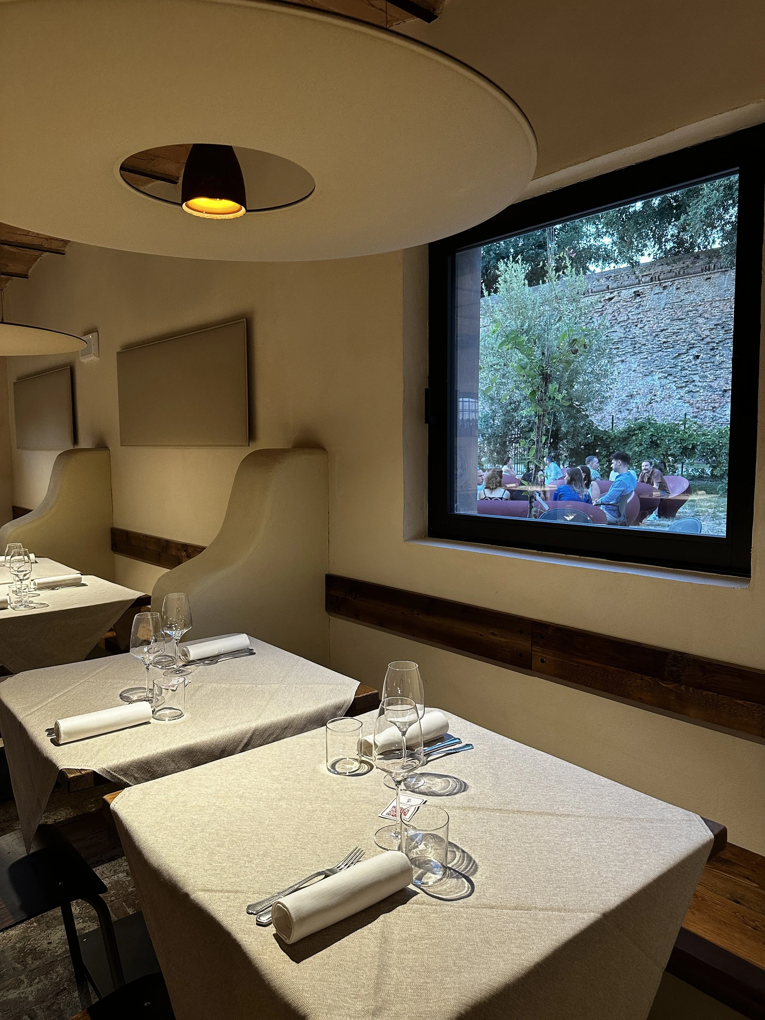 Tavola imbandita in un ristorante con bicchieri e posate, e vista al cortile esterno Casa dell'Ortolano con persone sedute al tavolo.