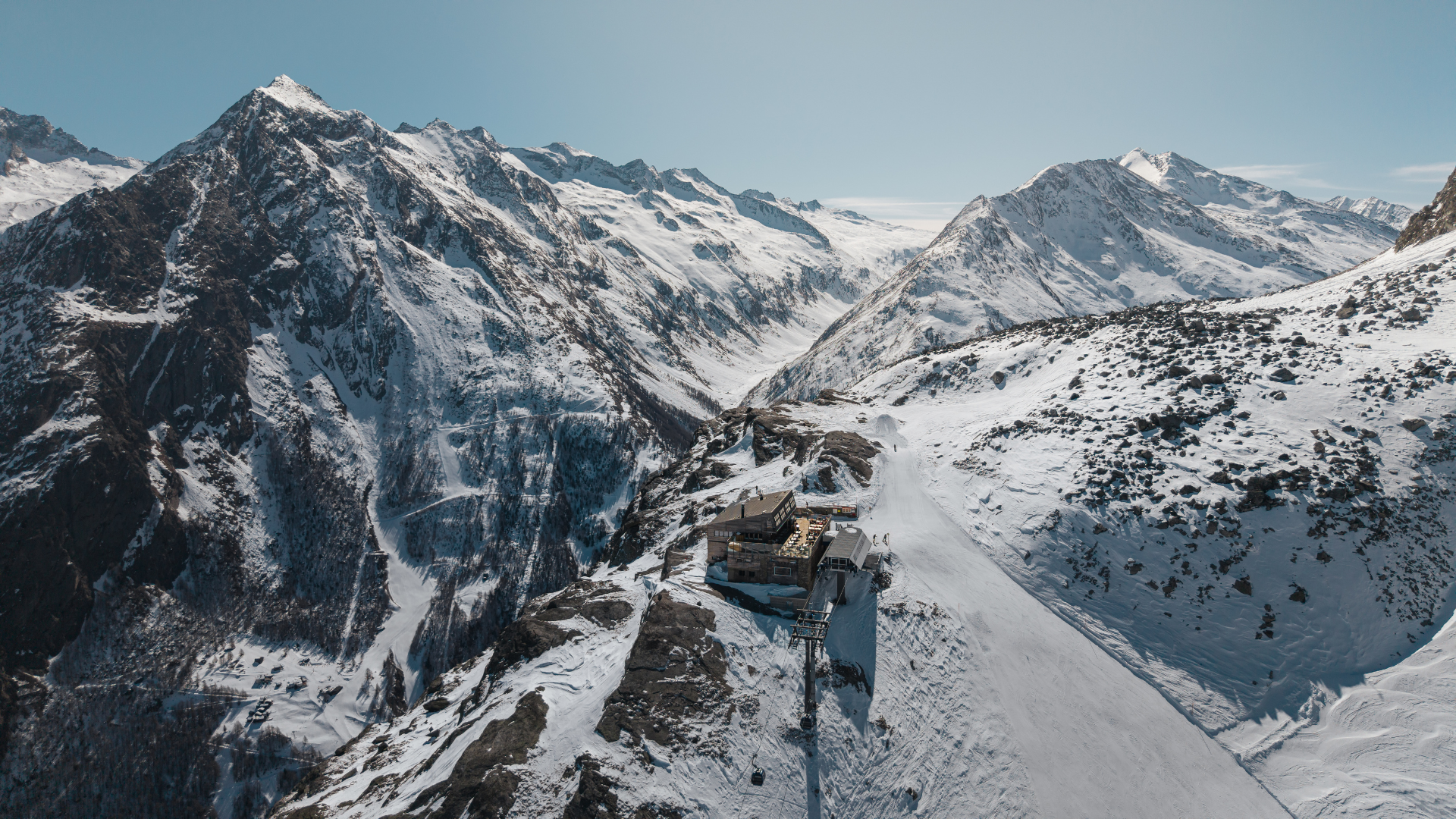 Schneebedeckte Berge in den Alpen mit einer Bergstation und Seilbahn im Vordergrund.