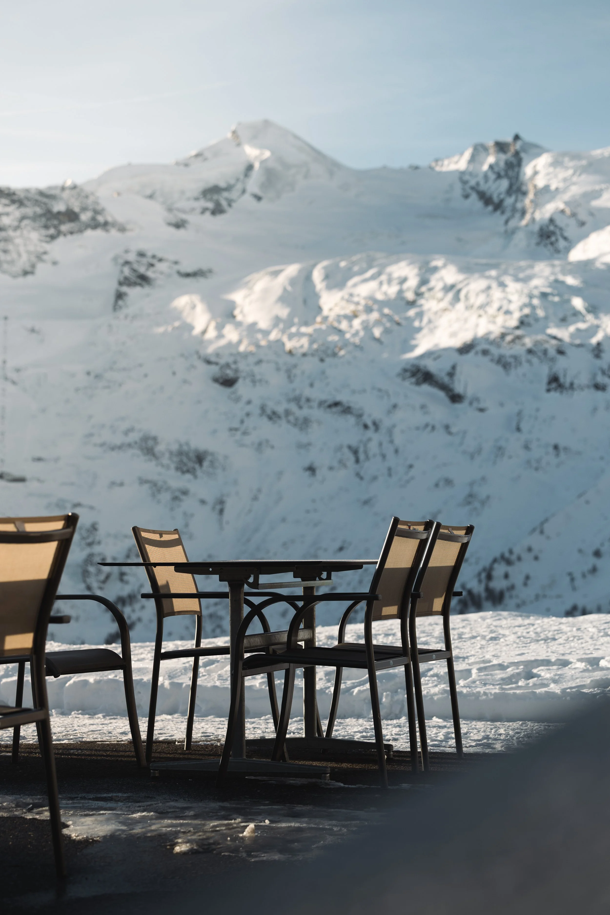 Sitzgelegenheiten im Freien vor einer verschneiten Berglandschaft mit hohen Gipfeln im Hintergrund.
