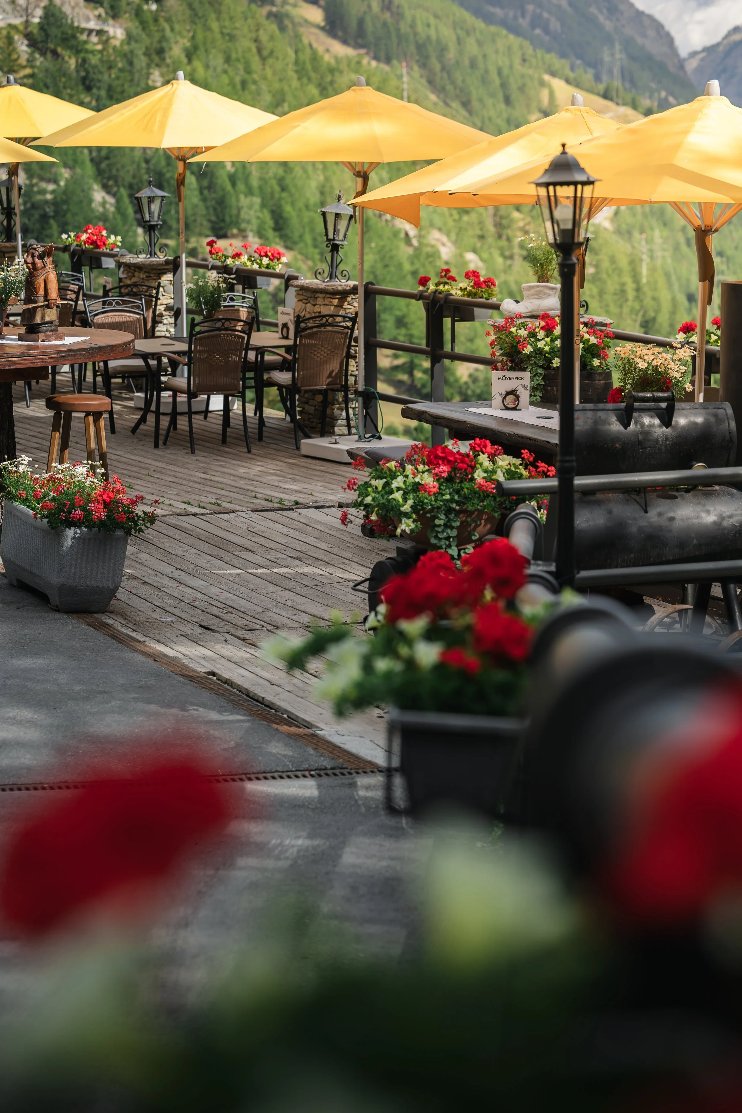 Bergige Landschaft mit einer Terrasse, gelben Sonnenschirmen, Blumen und Laternen, oberhalb eines Tals.
