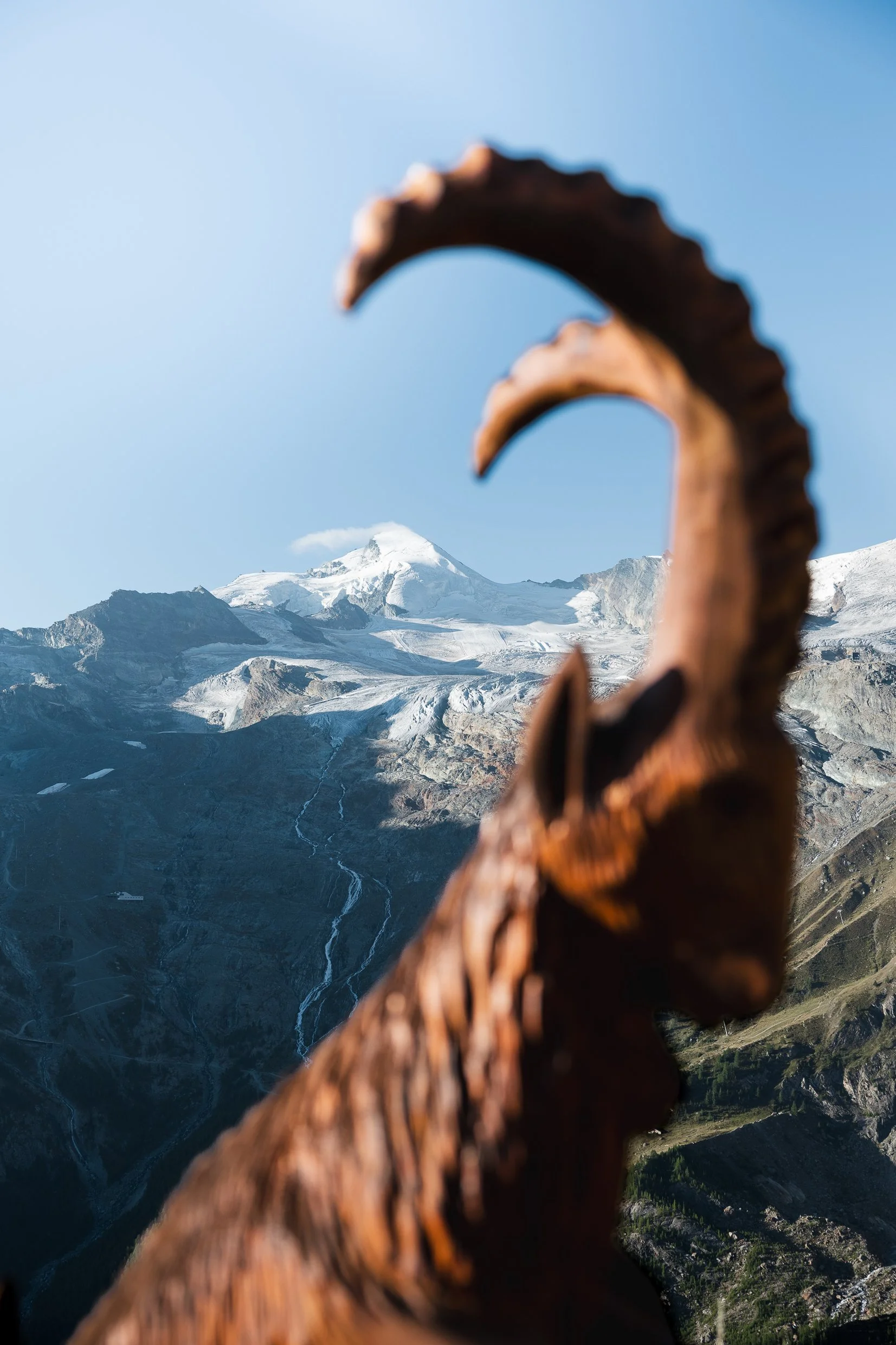 Blick auf schneebedeigte Berge mit Vulkan, im Vordergrund eine verwitterte Holzfigur