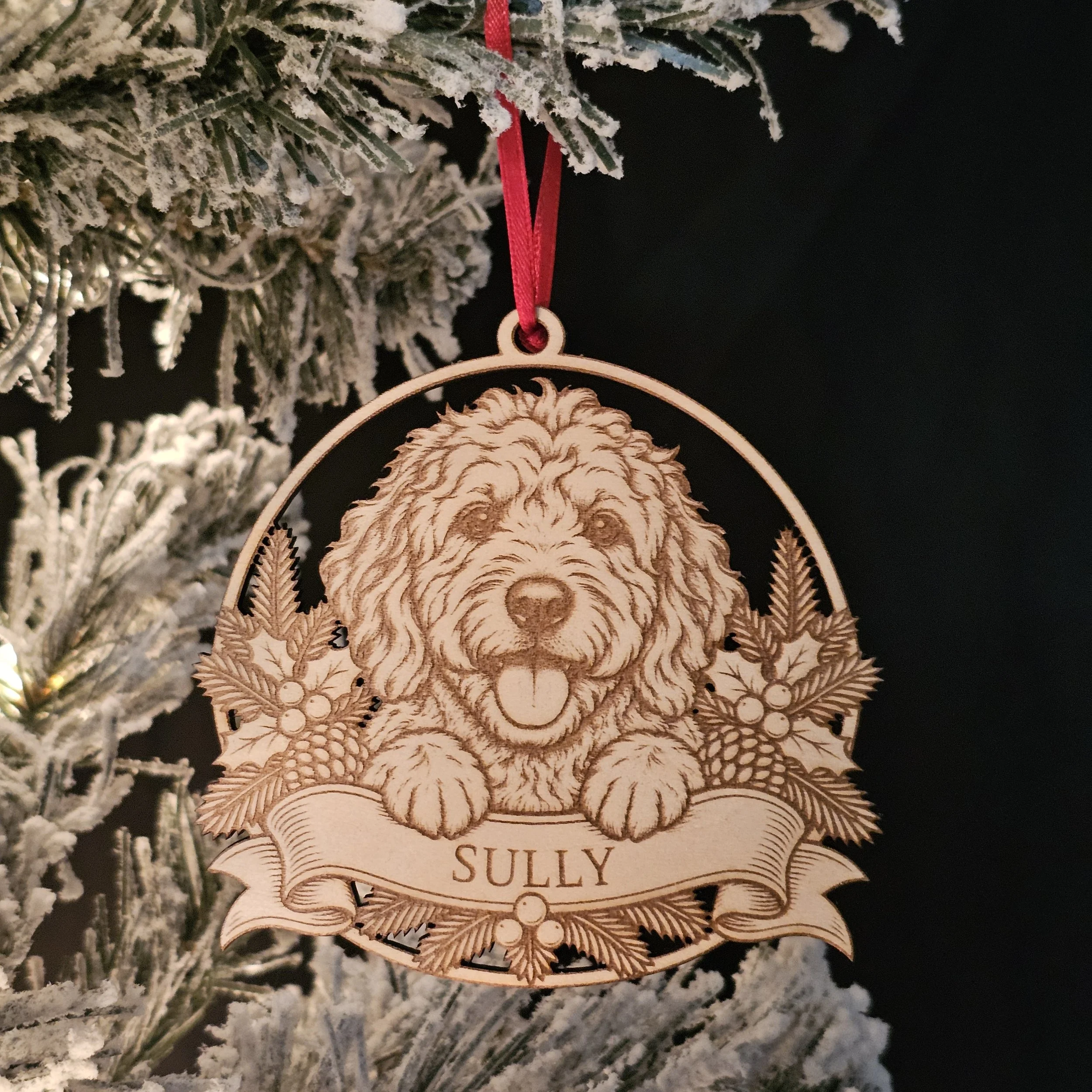 Goldendoodle ornament with name hanging on snowy warm Christmas Tree.