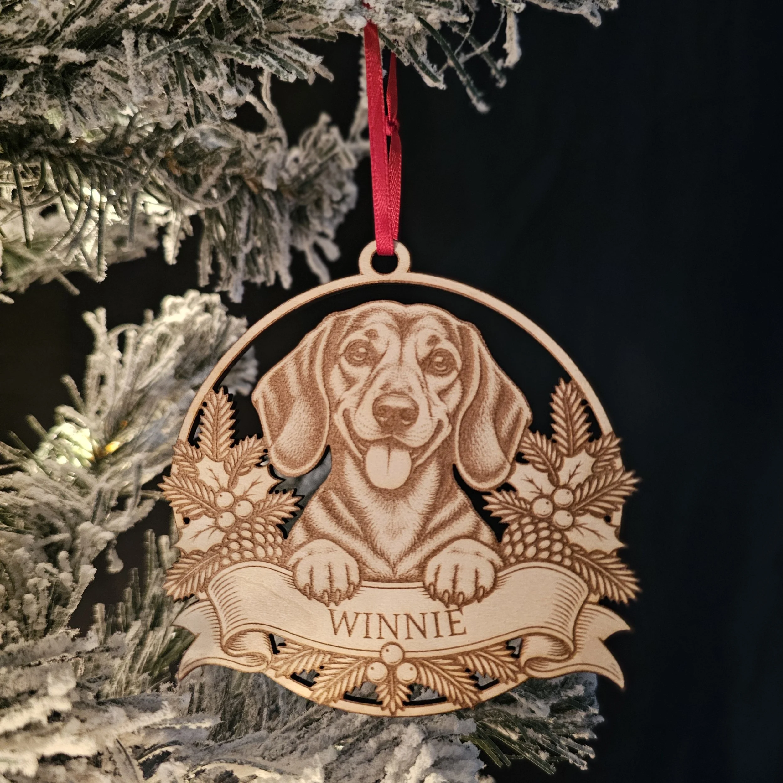 Dachshund ornament with name hanging on snowy warm Christmas Tree.