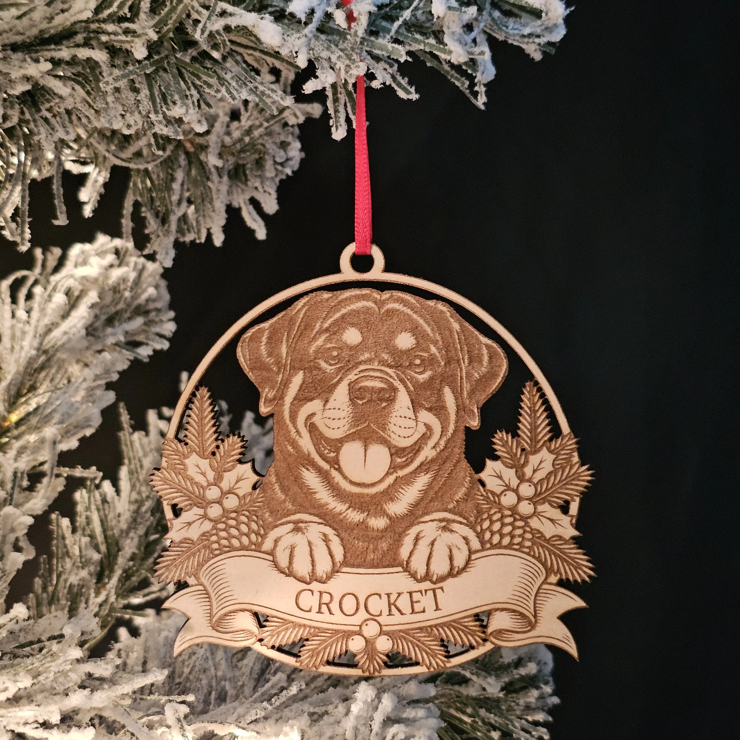 Rottweiler ornament with name hanging on snowy warm Christmas Tree.