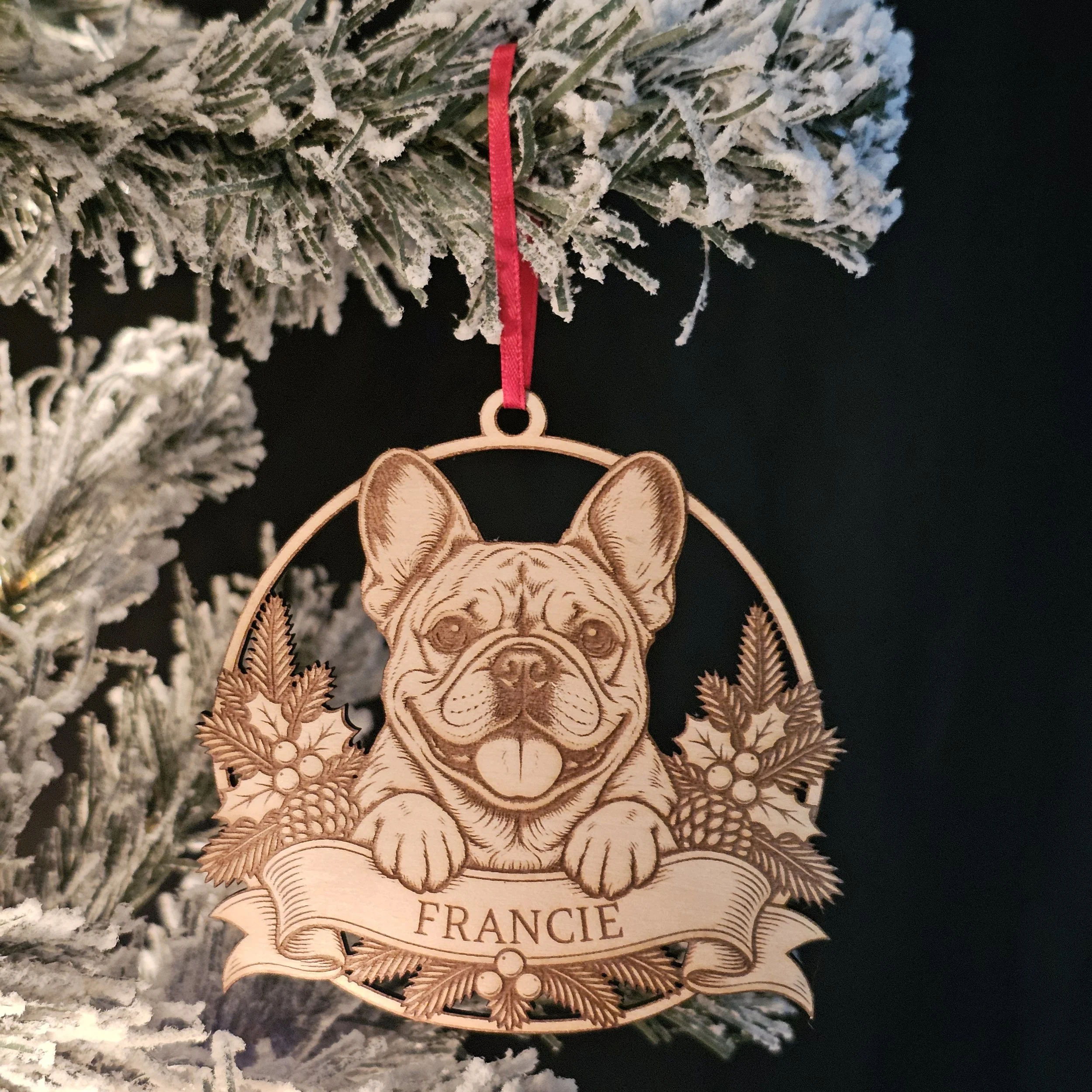 French Bulldog ornament with name hanging on snowy warm Christmas Tree.