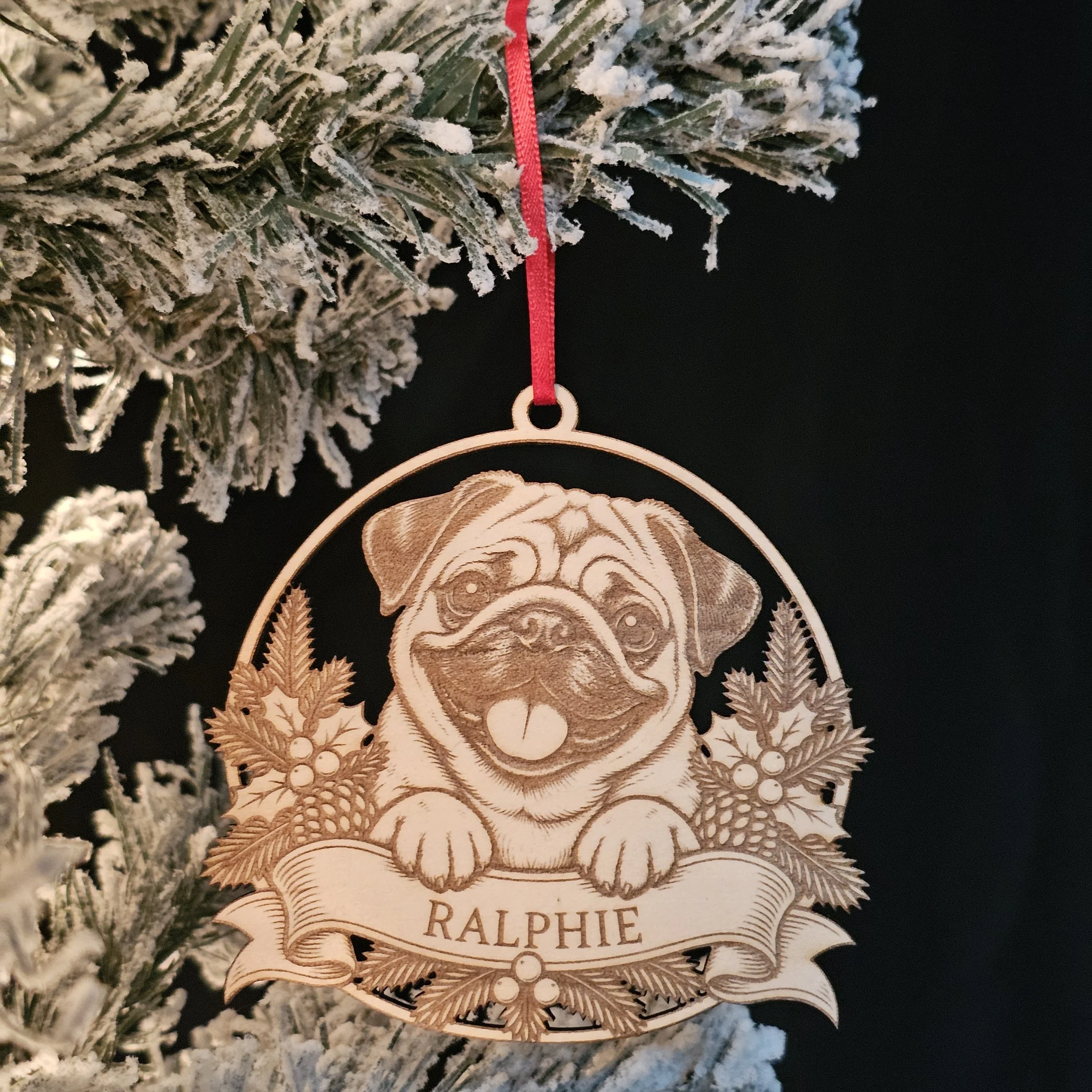 Pug ornament with name hanging on snowy warm Christmas Tree.