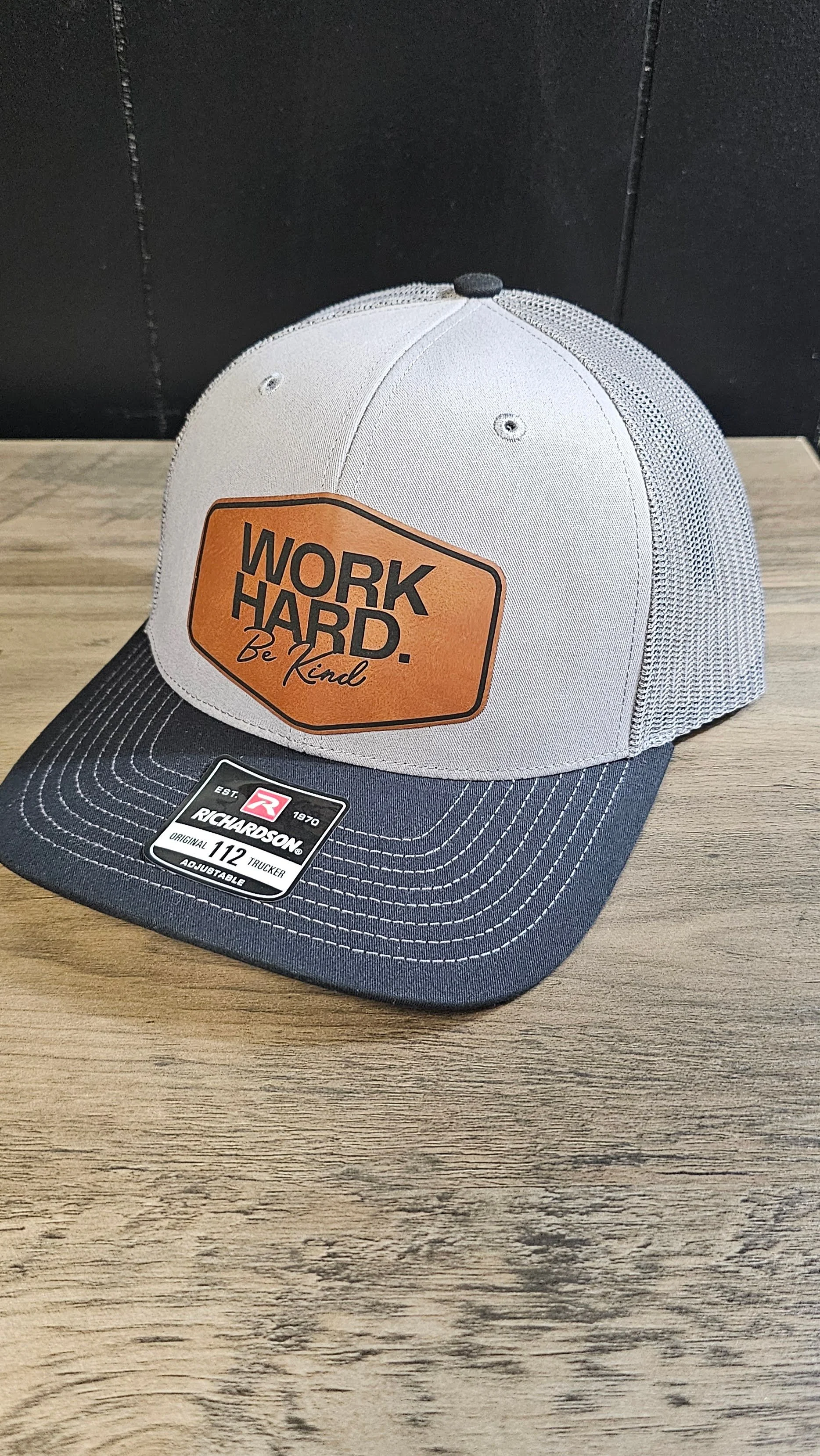 A Richardson hat with a leatherette patch including "Work Hard, Be Kind" for a local real estate agent
