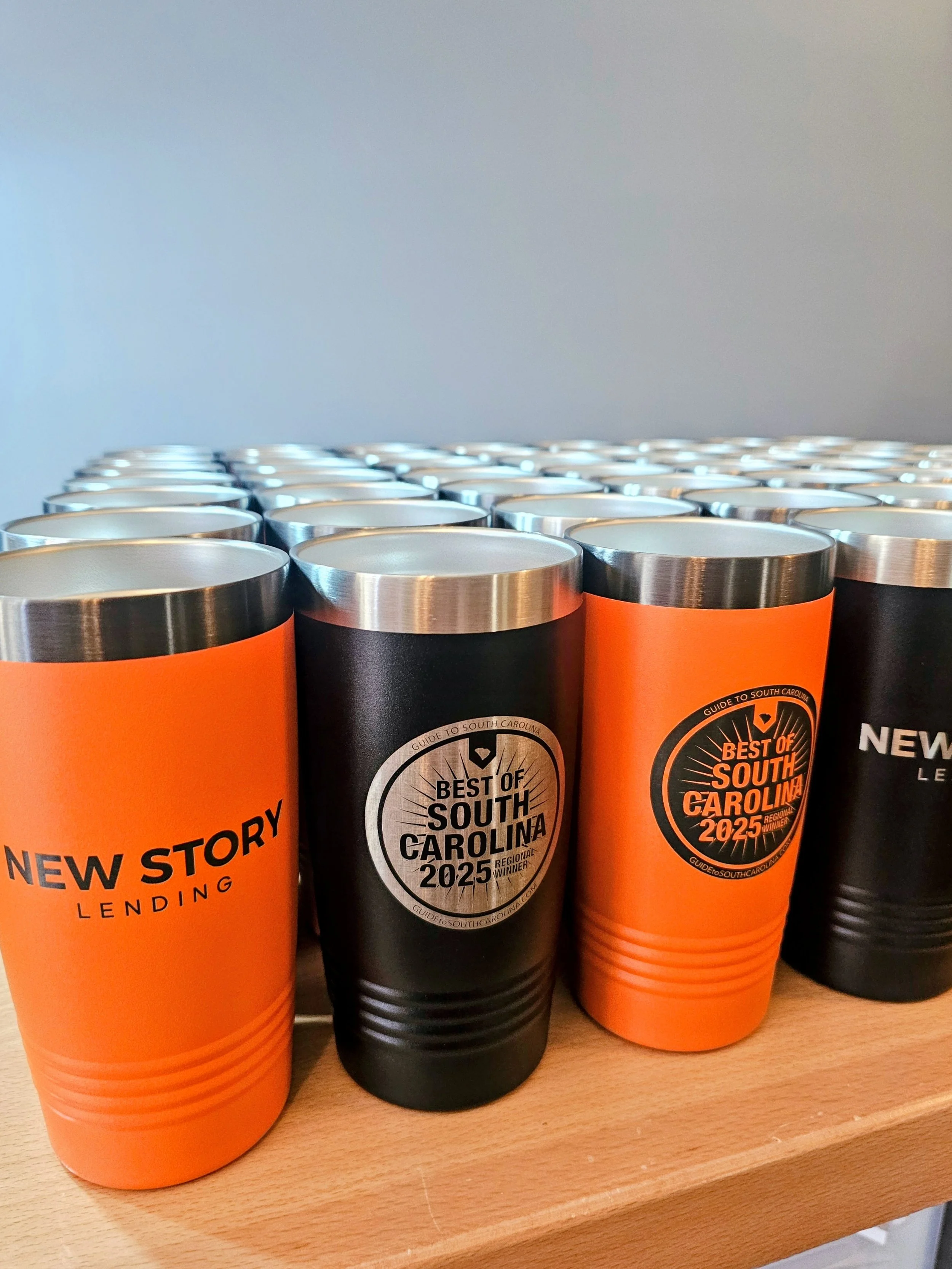 A batch of black and orange tumblers engraved with a local lender's logo and award designation