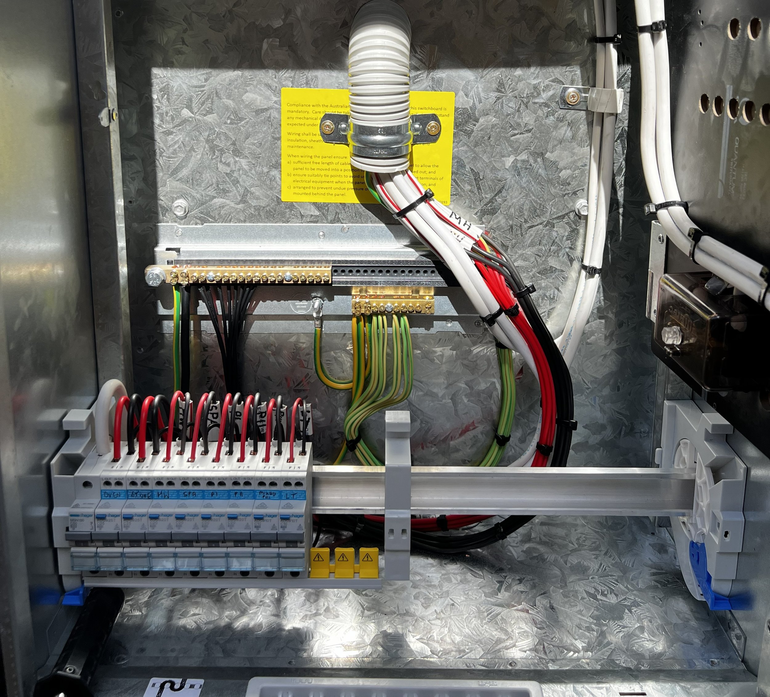 Electrical panel with wiring, circuit breakers, and a yellow warning label inside an industrial metal enclosure.