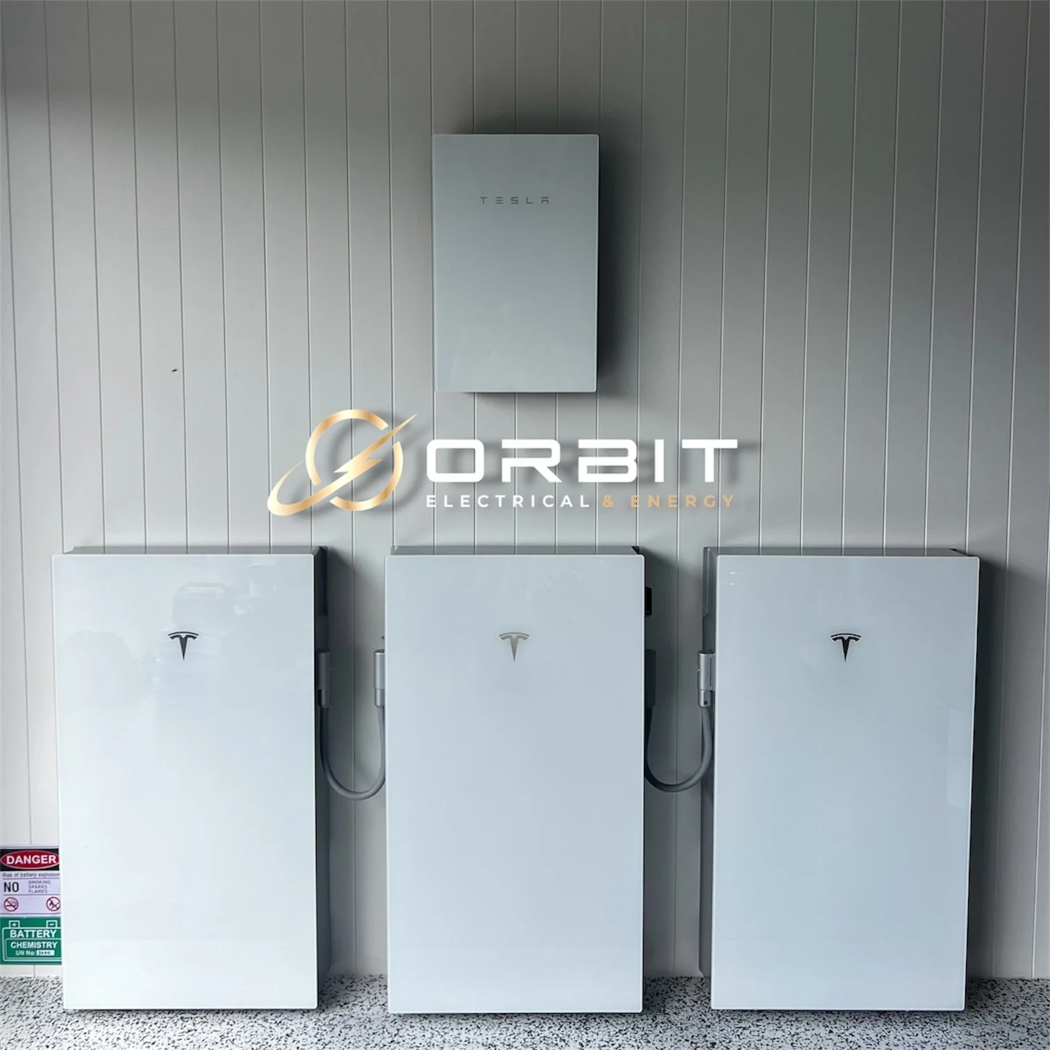 Three Tesla Powerwall batteries mounted on a wall with a Tesla solar inverter above them, and a logo of Orbit Electrical & Energy across the middle of the image.
