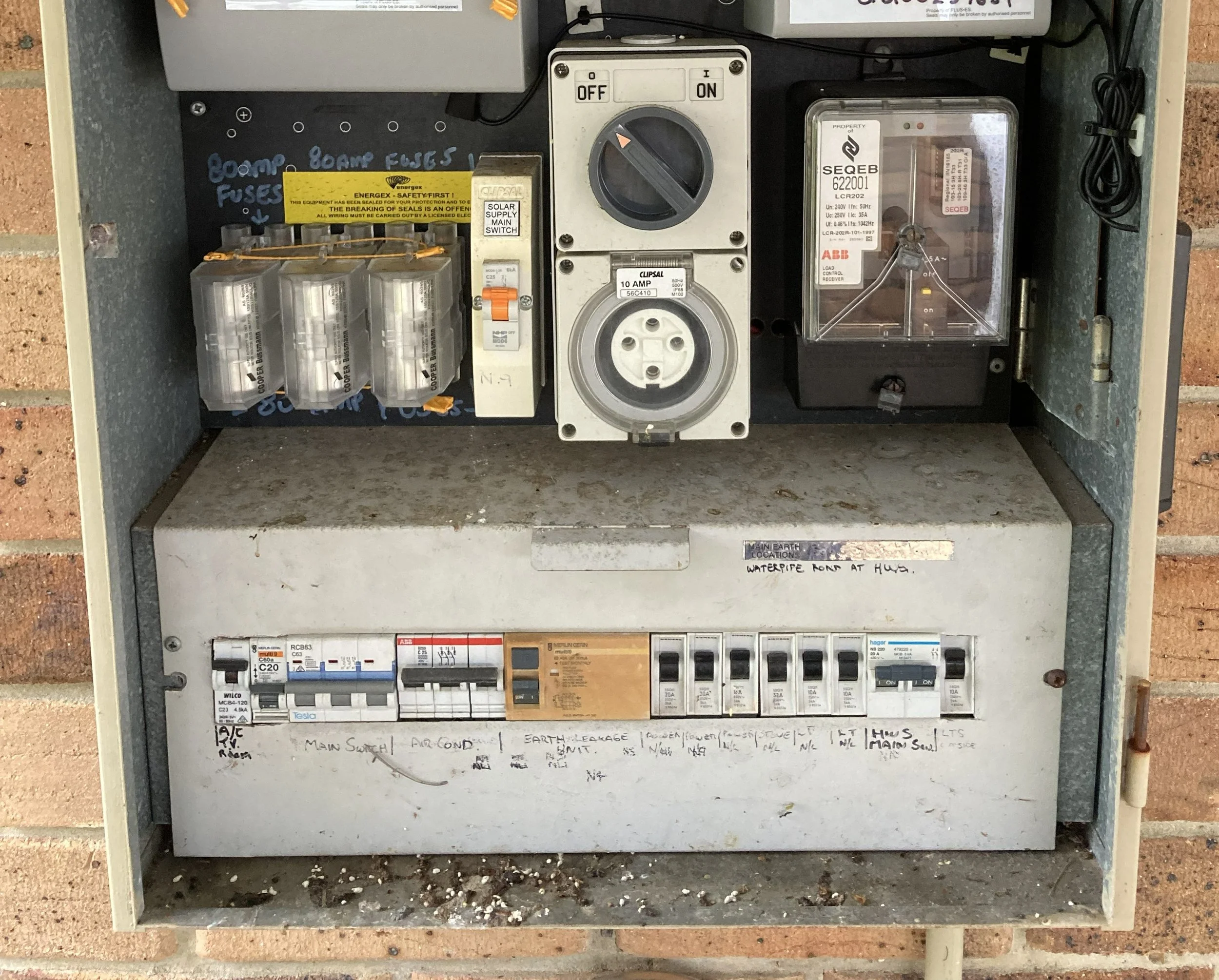 Electrical panel with various switches, circuit breakers, and a fuse box mounted inside a metal enclosure. Handwritten labels and notes are visible on the panel, including fuse and earth leakage warnings.