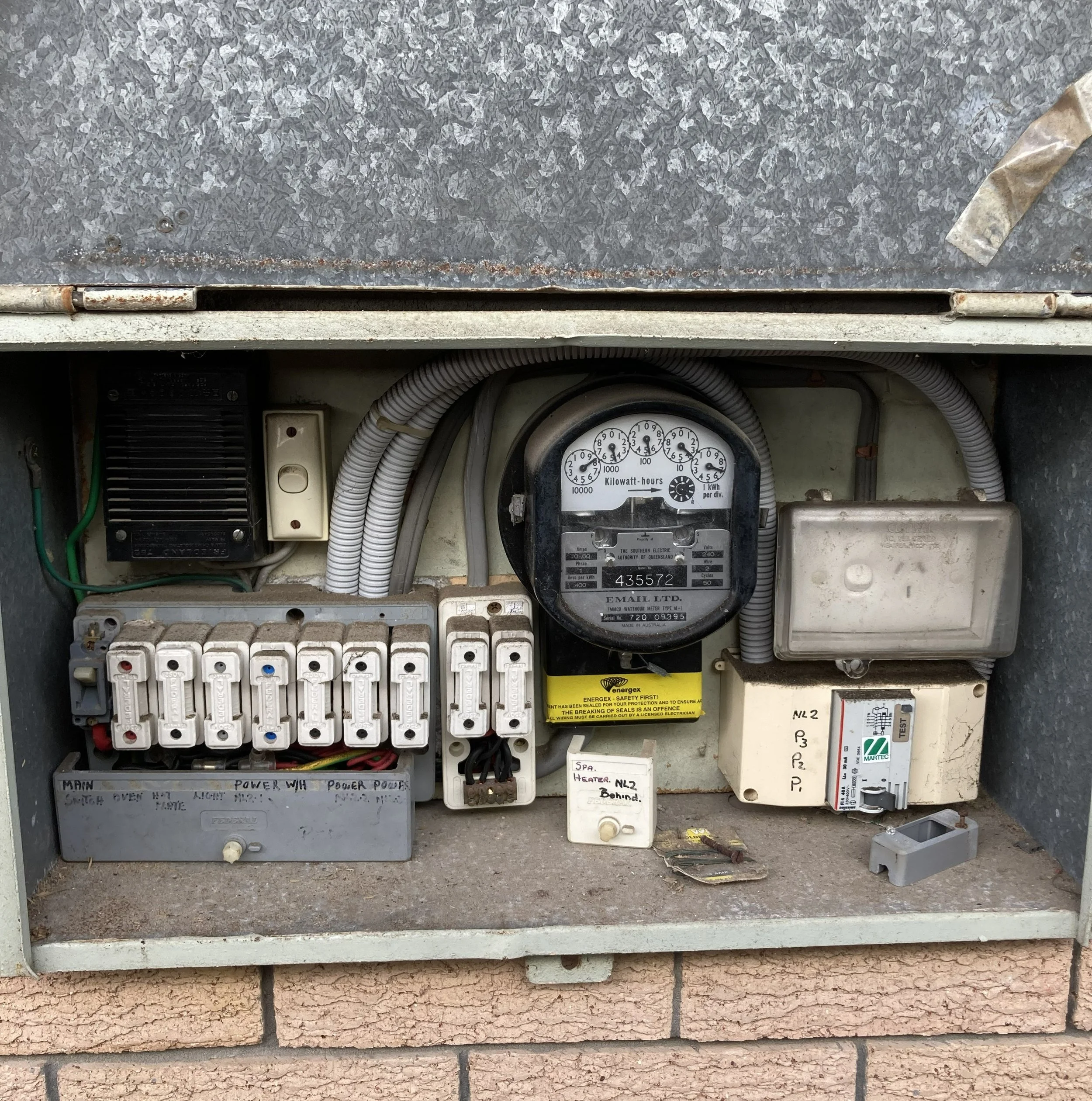 Close-up of an electrical meter box with multiple wires and a power meter, installed on a brick wall.