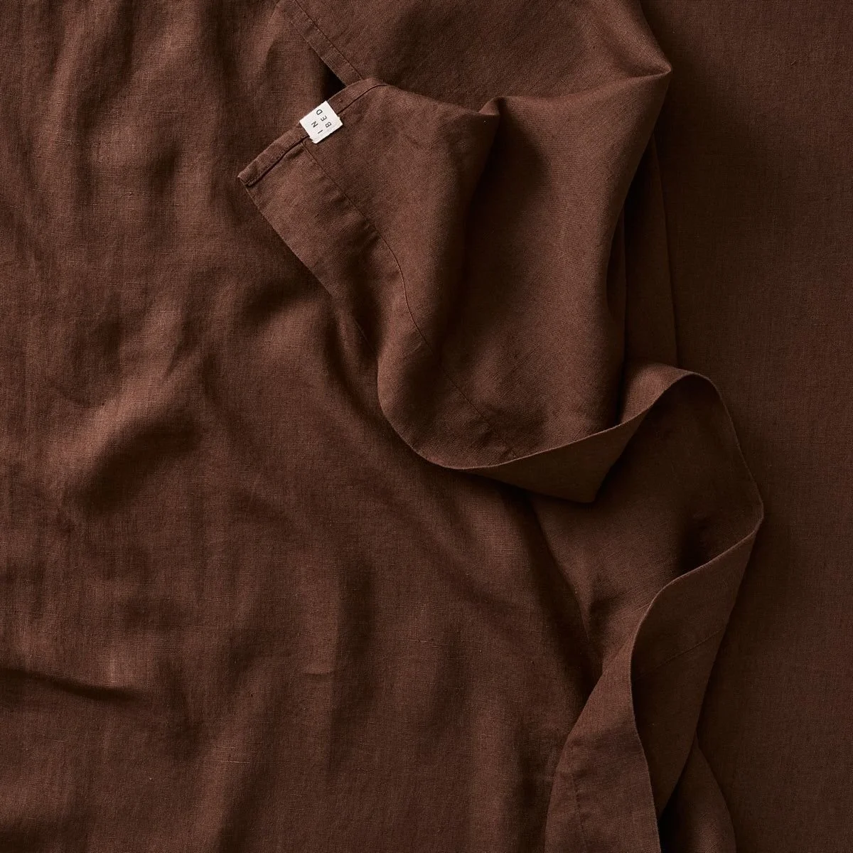 Close-up of rumpled brown linen fabric with a sewn white label and draped edge