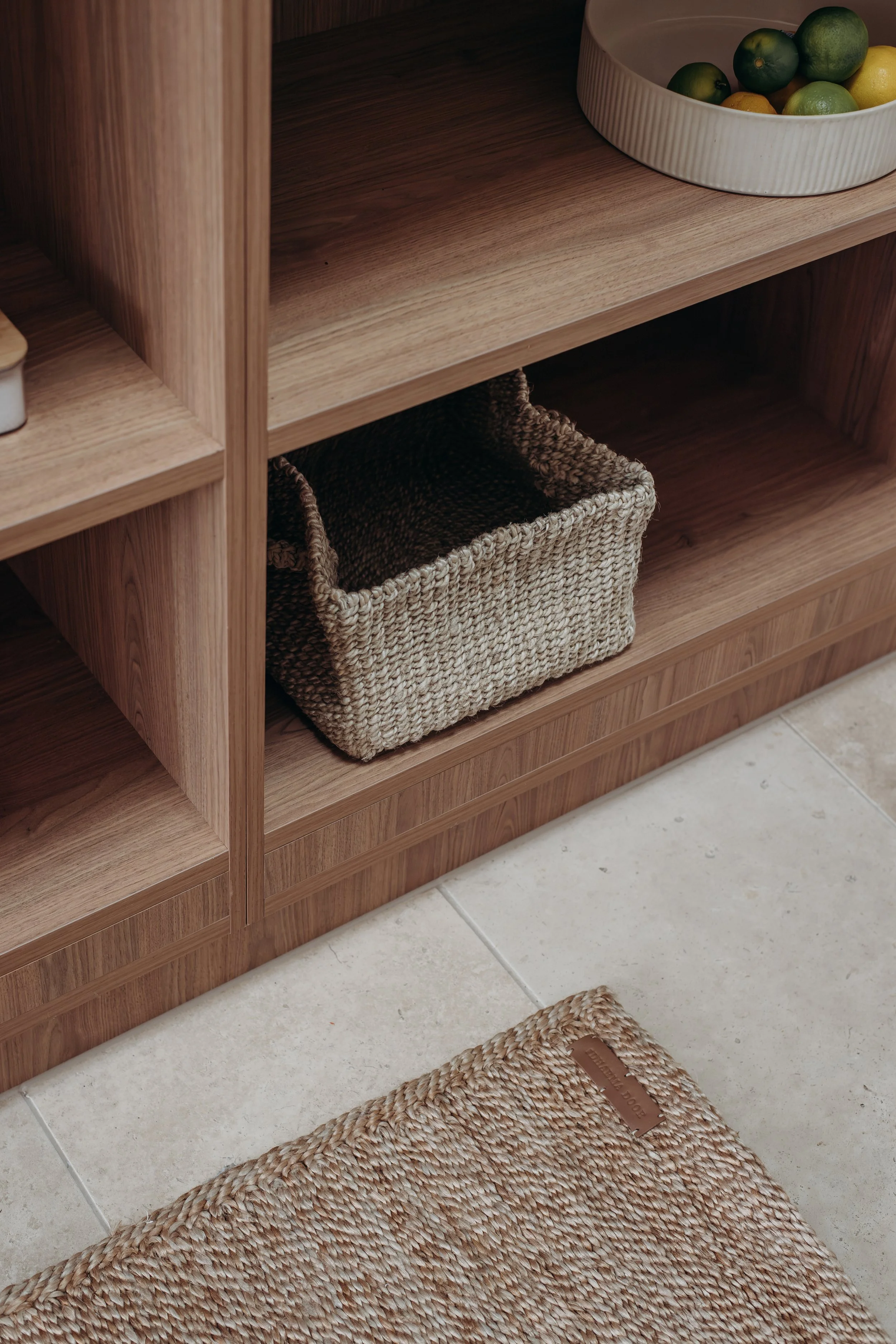 Wooden shelving unit with woven storage baskets and a white bowl of citrus fruit