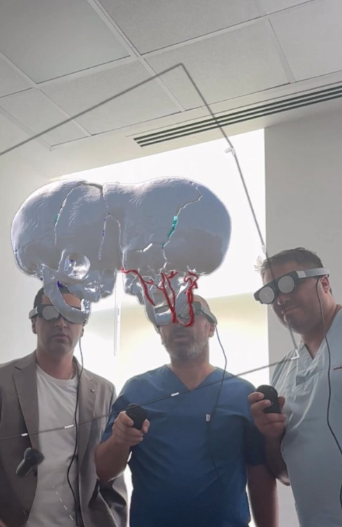 Three men in a medical or research setting wearing virtual reality headsets looking at a simulation of a human skull suspended in midair.