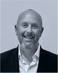 Black and white portrait of a smiling man with a beard, wearing a suit jacket and collared shirt.