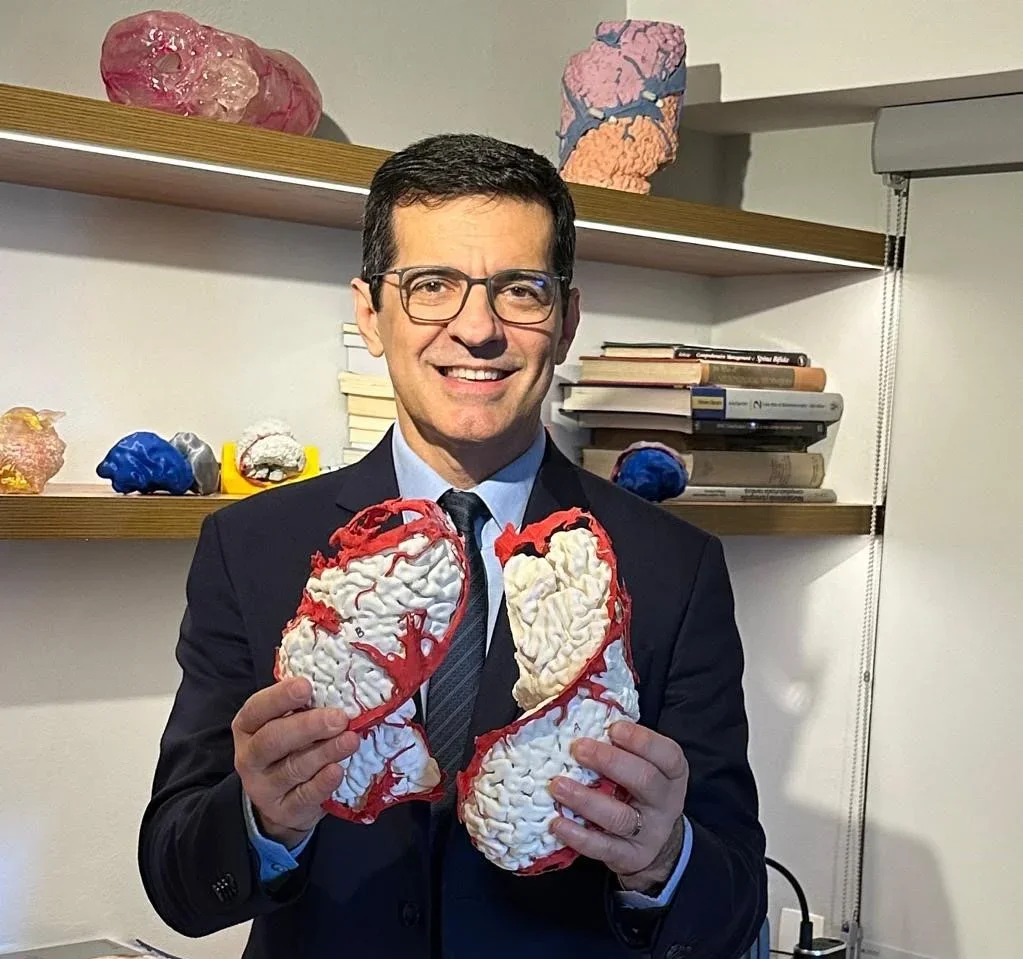 A man in a suit holding two realistic-looking brain models in his hands, smiling at the camera.