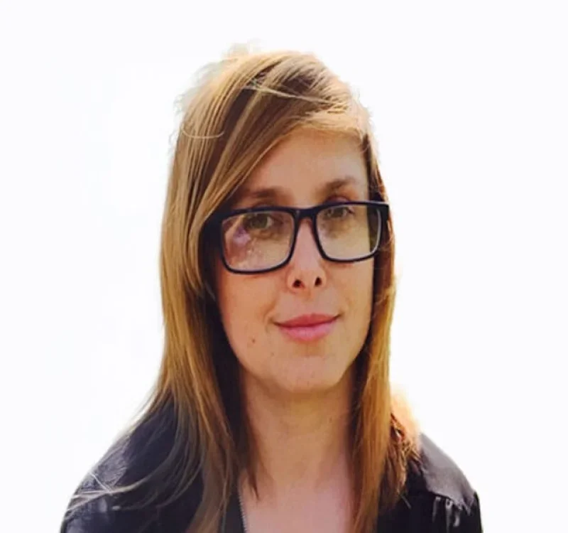 A woman with long light brown hair wearing glasses, looking at the camera with a slight smile.
