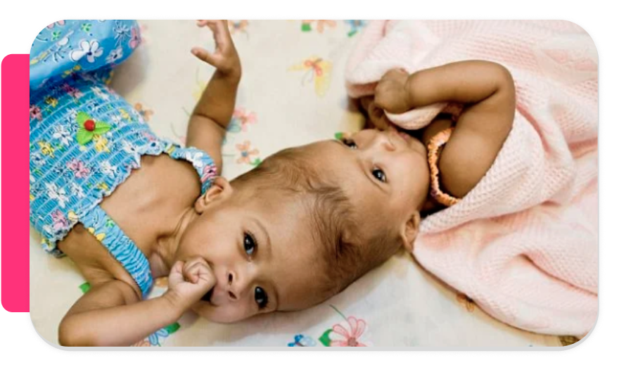 Two babies lying on a patterned blanket, one is sucking on her thumb and the other is resting her head on her arm wrapped in a blanket.