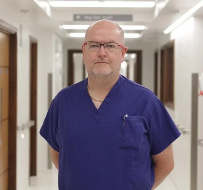 A man in navy medical scrubs standing in a hospital hallway.