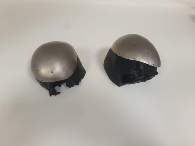 Two black and silver metallic objects, possibly shell or helmet parts, placed on a white surface.