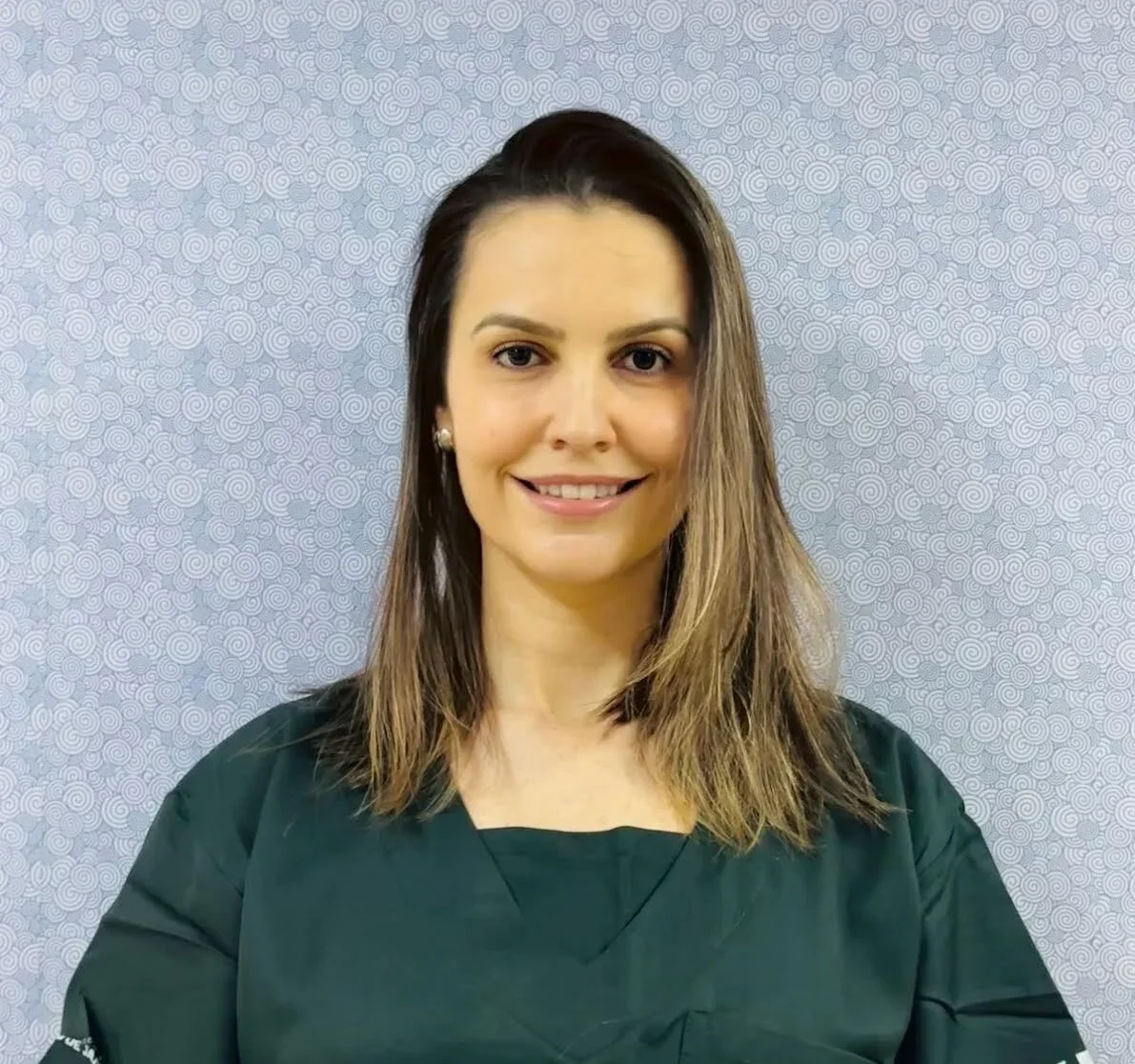 A woman with shoulder-length brown hair smiling at the camera, wearing a green top, against a textured gray background.