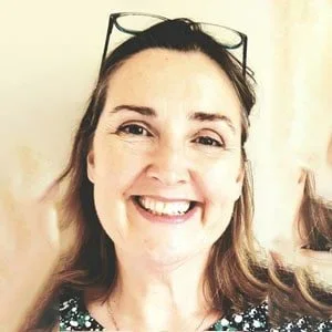 A woman smiling with sunglasses resting on her head, wearing a patterned top.