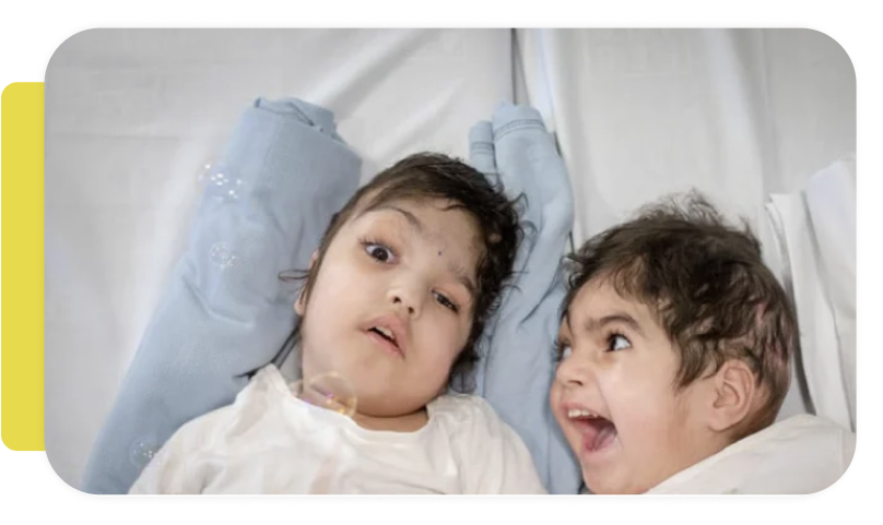 Two children lying in hospital beds, one with a serious expression and the other smiling.