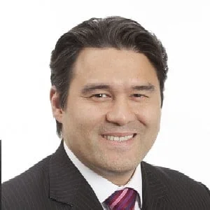Portrait of a man with dark hair in a suit and tie smiling at the camera.
