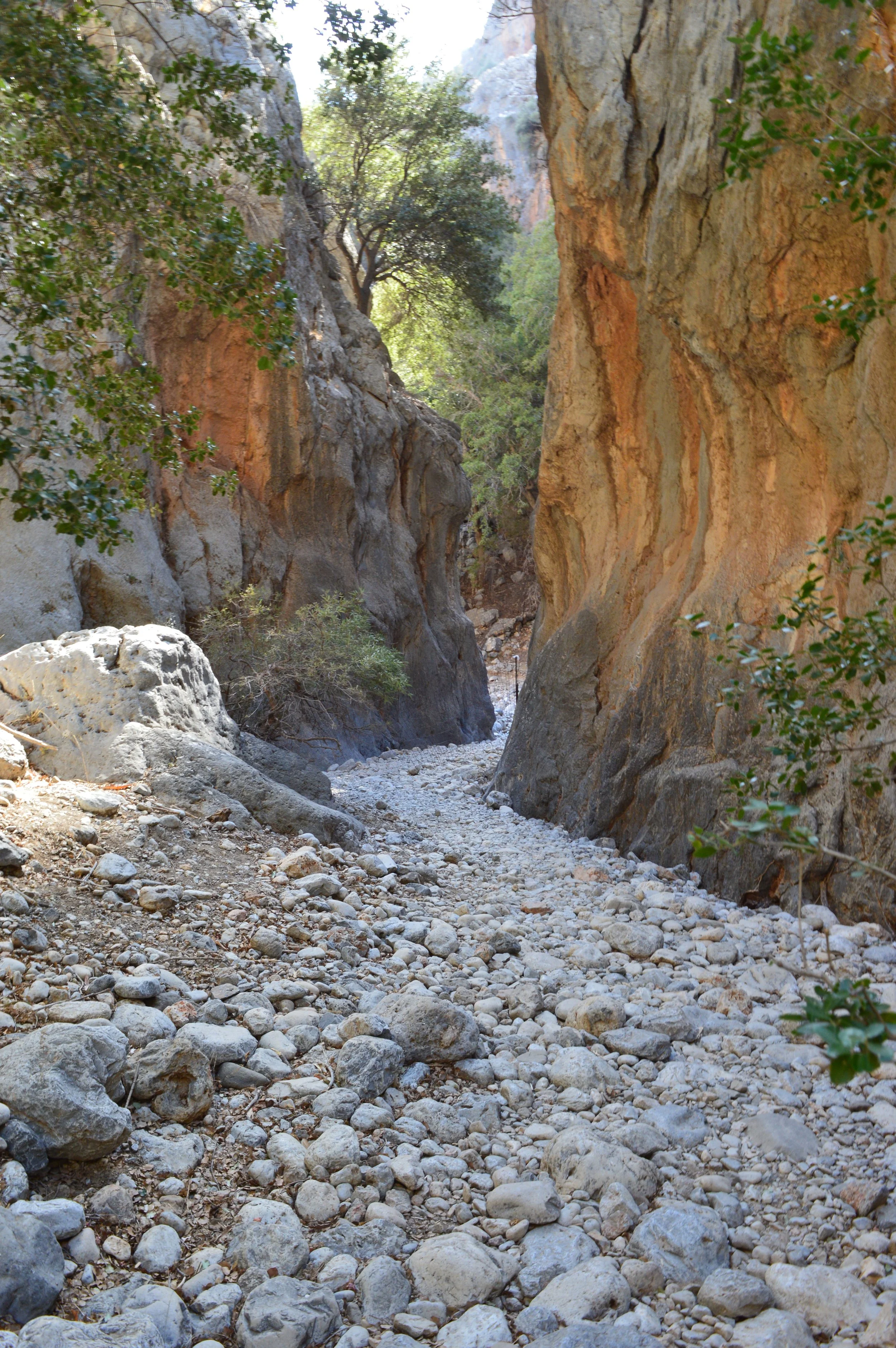 Milatos Garden Villas -  kritsa gorge-A rocky canyon with dry, gravelly floor and steep, rugged canyon walls on either side, with some trees and green bushes along the top edges of the canyon.