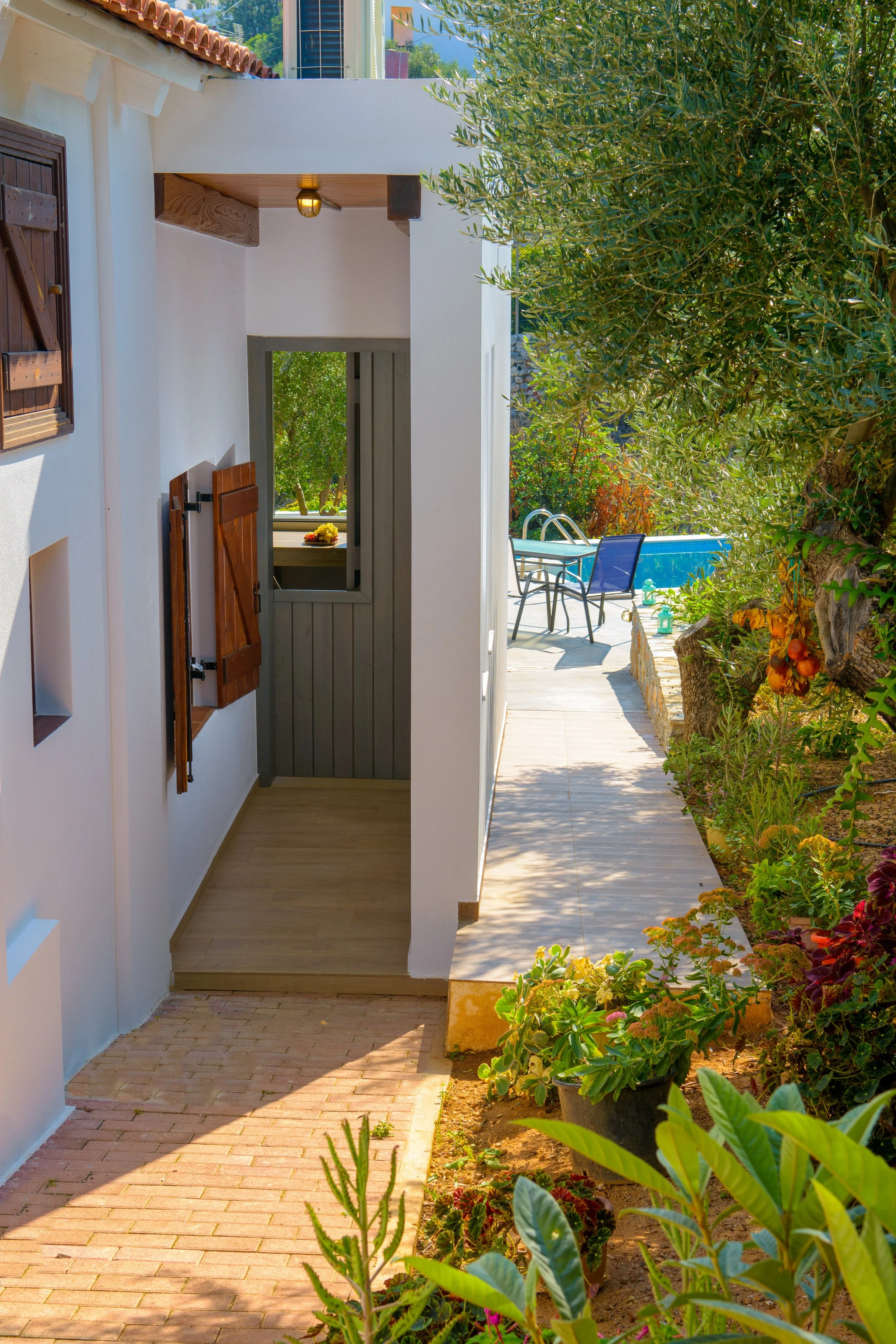 An outdoor patio area with a swimming pool in the background, surrounded by lush greenery and colorful plants, with a small table and chairs nearby.