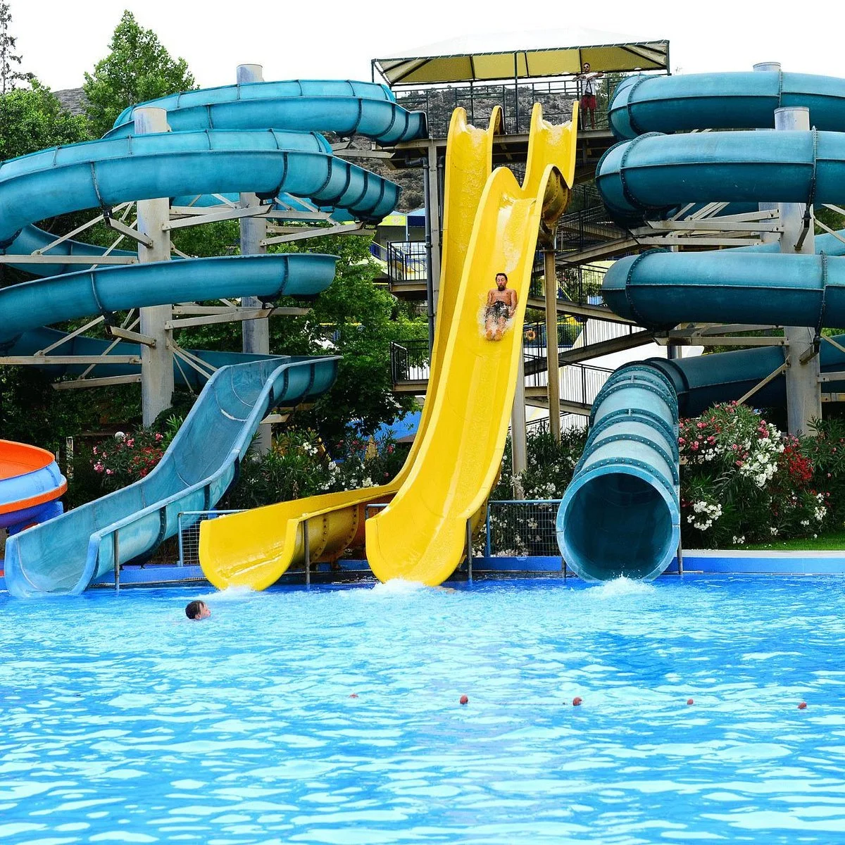 People enjoying water slides at a water park, with one person sliding down a yellow slide and going into a swimming pool.