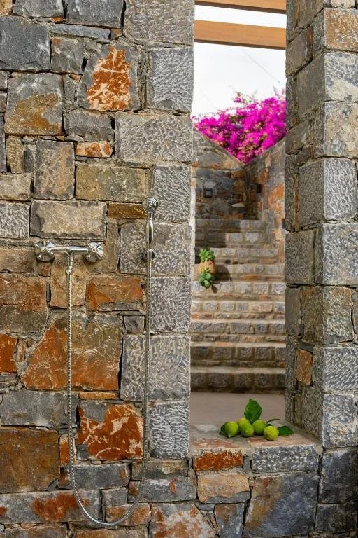 Milatos Garden Villas - Stone shower area with two metal showerheads and a stepped outdoor space with pink flowers and green limes.