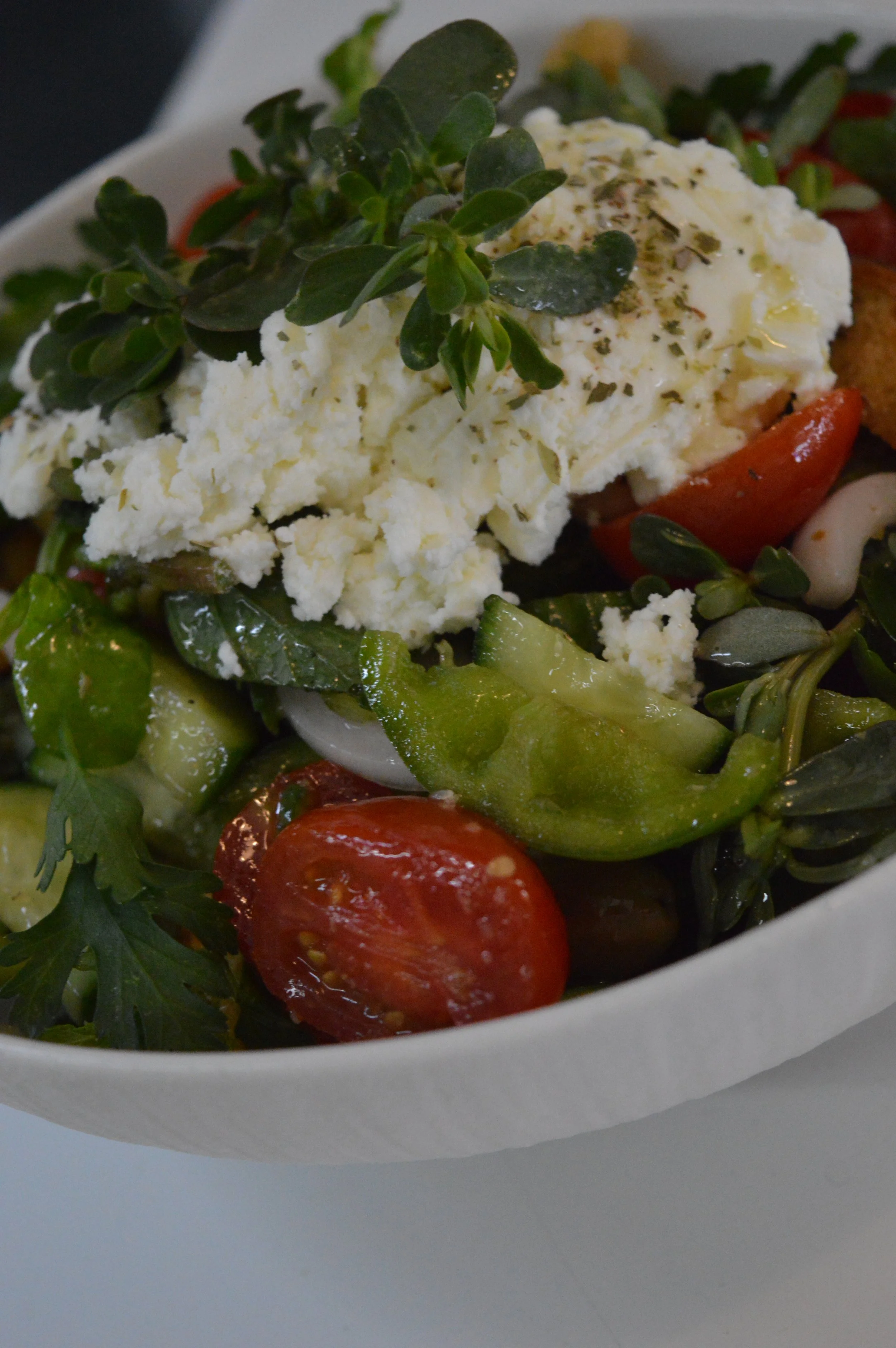 Fresh salad with cherry tomatoes, cucumber, leafy greens, topped with crumbled feta cheese and herbs.