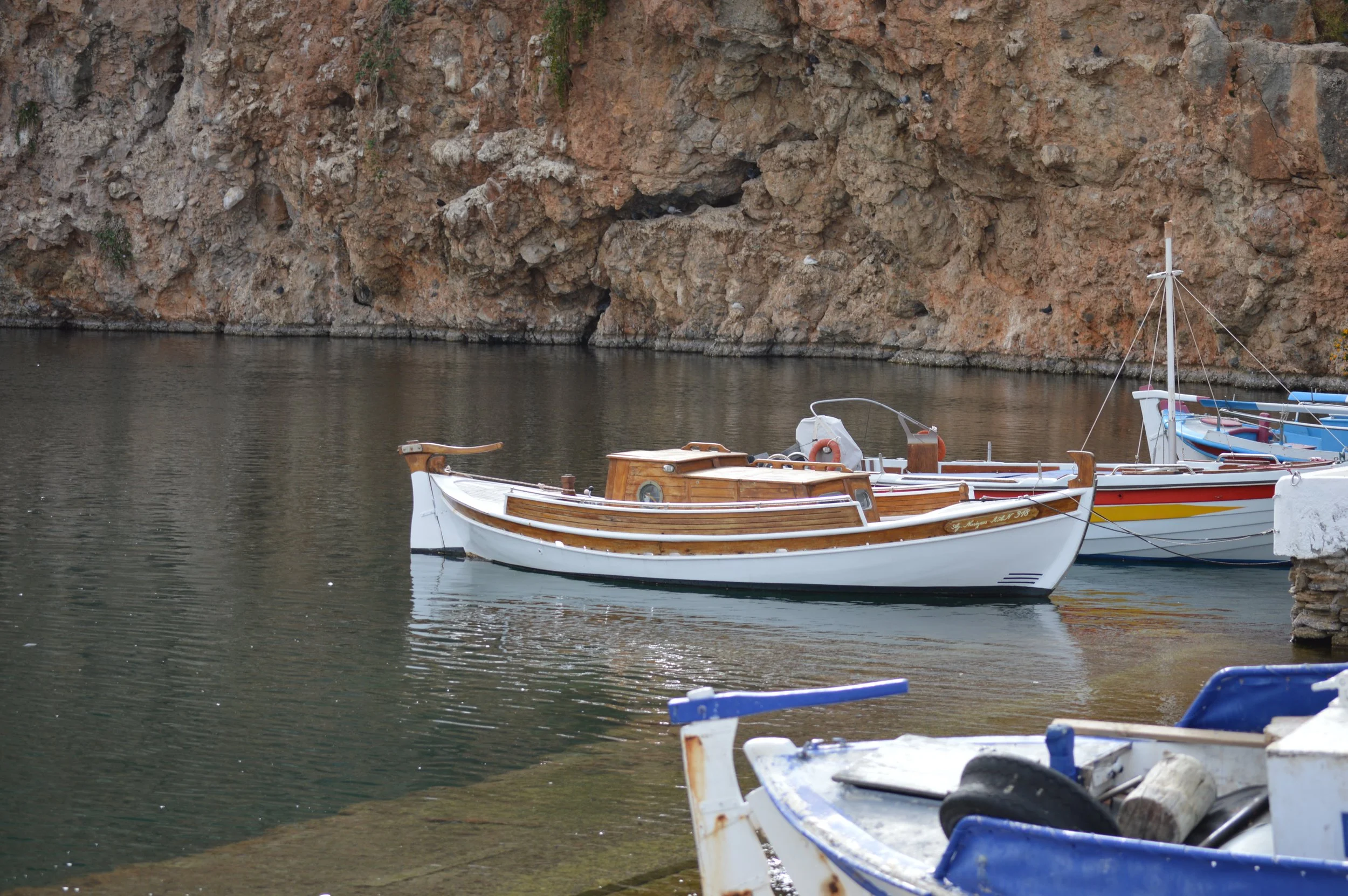 Several small boats docked near a rocky shoreline with cliffs.