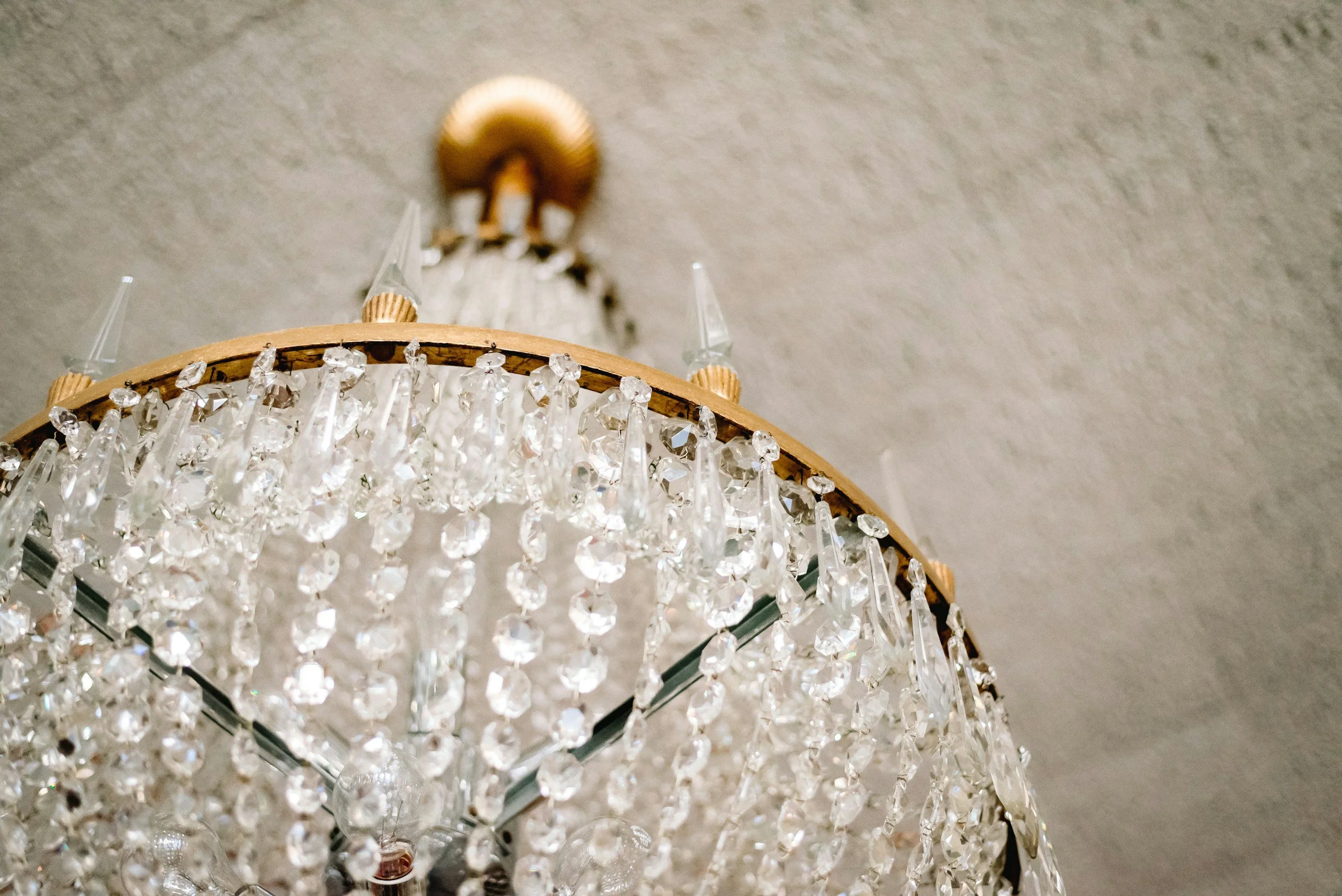 Close-up of a chandelier with crystal decorations hanging from a circular wooden frame, viewed from below against a plain ceiling.