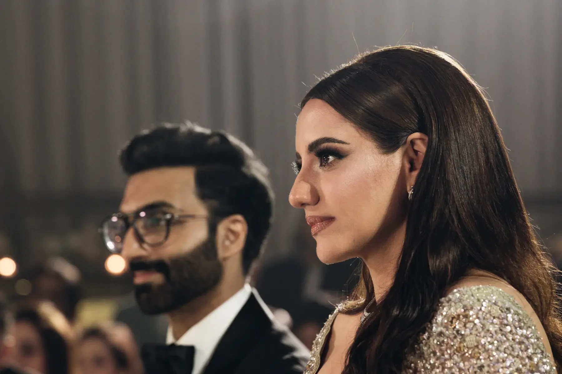 A woman with long dark hair and a man with glasses and a beard, dressed in formal attire, participating in a formal event.