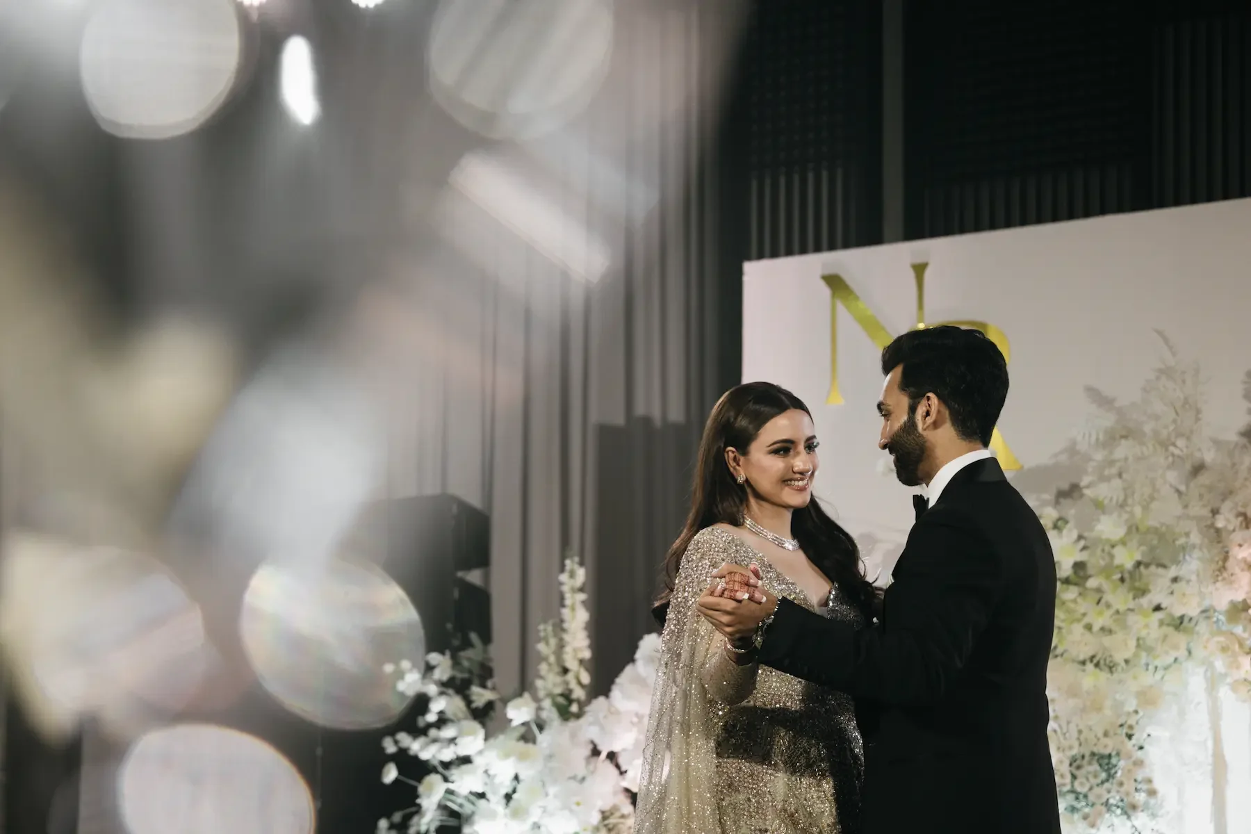 A bride and groom dancing at their wedding reception, with a floral backdrop and elegant decorations.