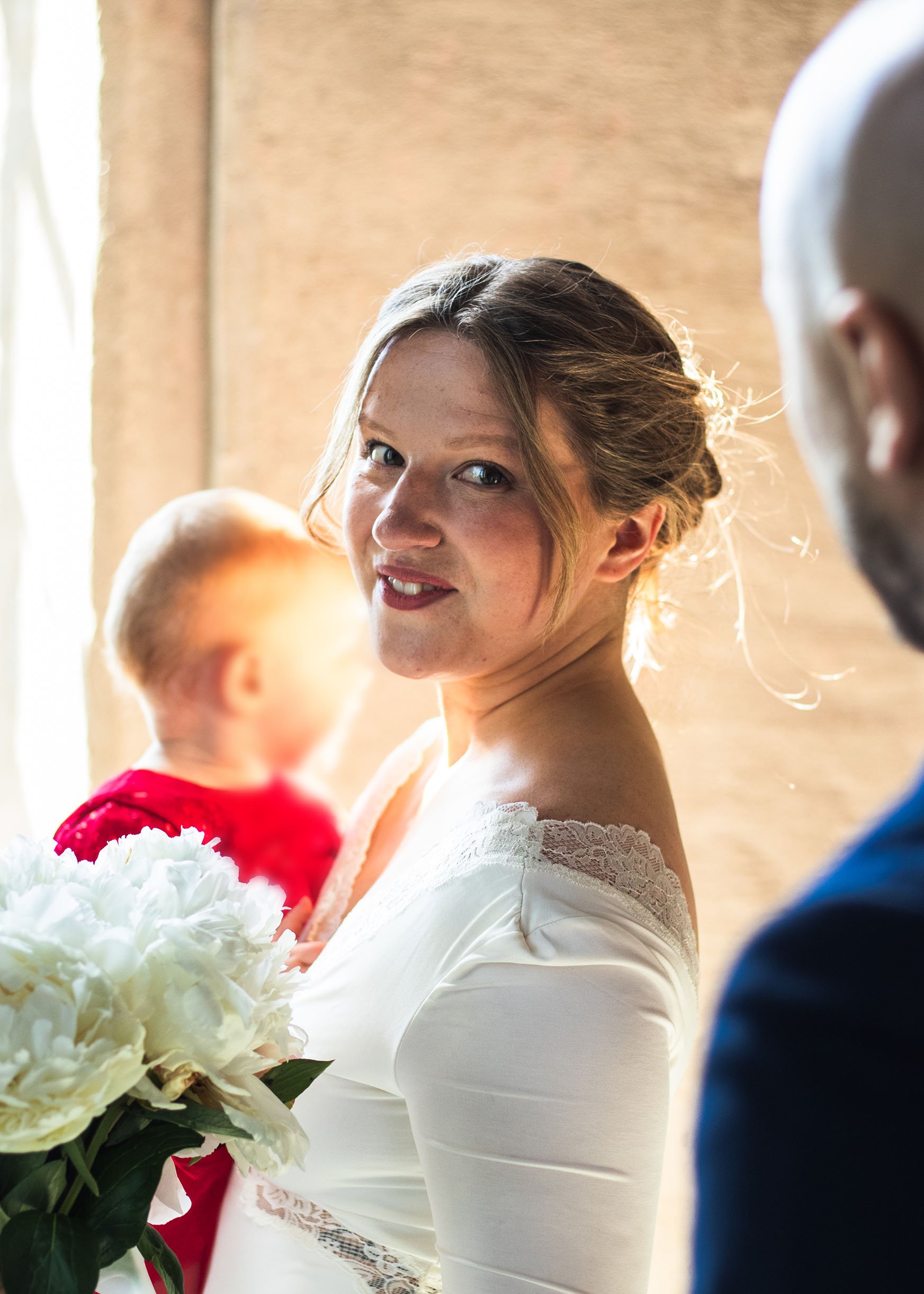 En kvinna i vit klänning som håller ett bukett av vita och röda blommor, hon tittar bakåt och ler.