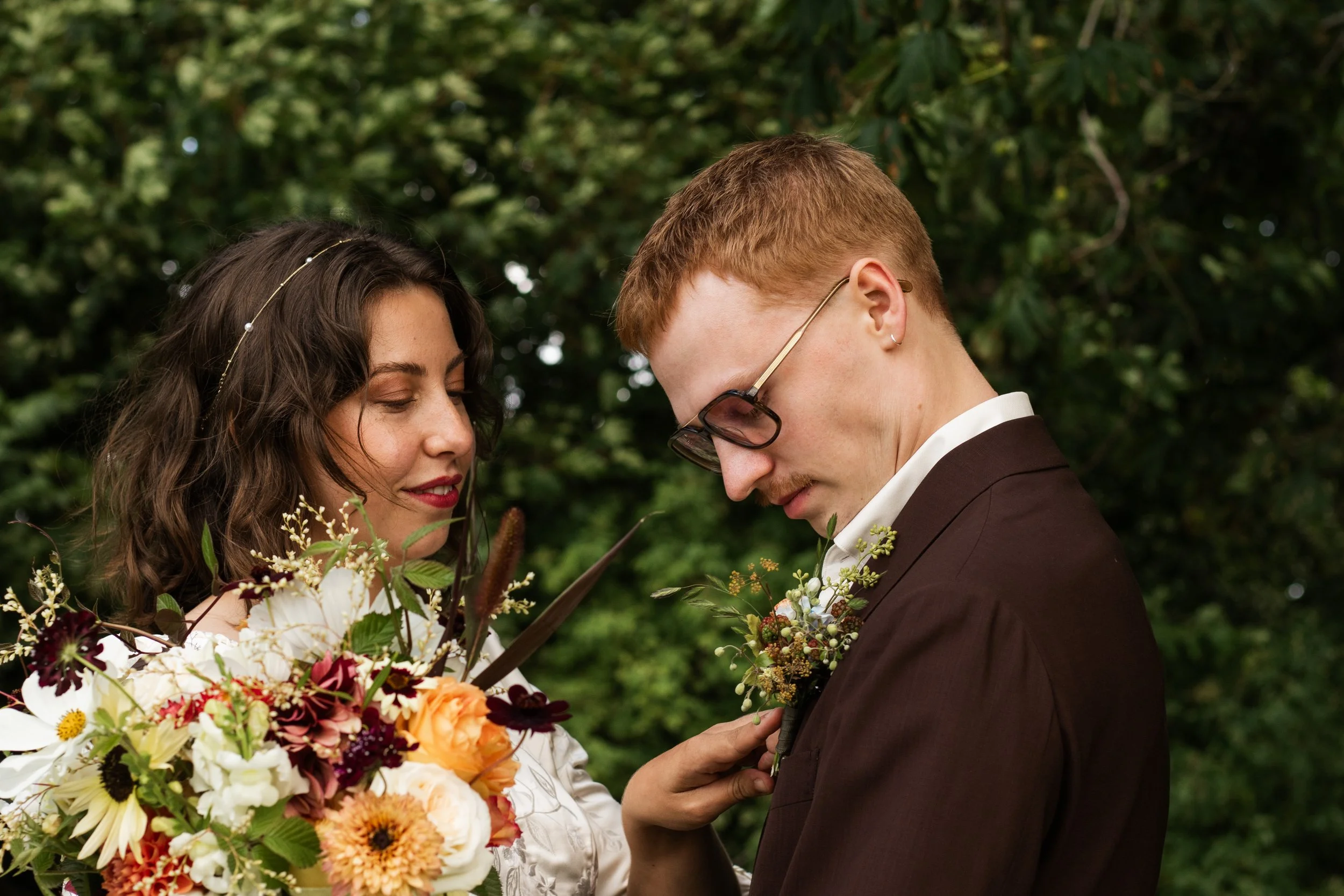 Ungt par som är gifta, står nära varandra, omgiven av blommor i en utomhusmiljö.