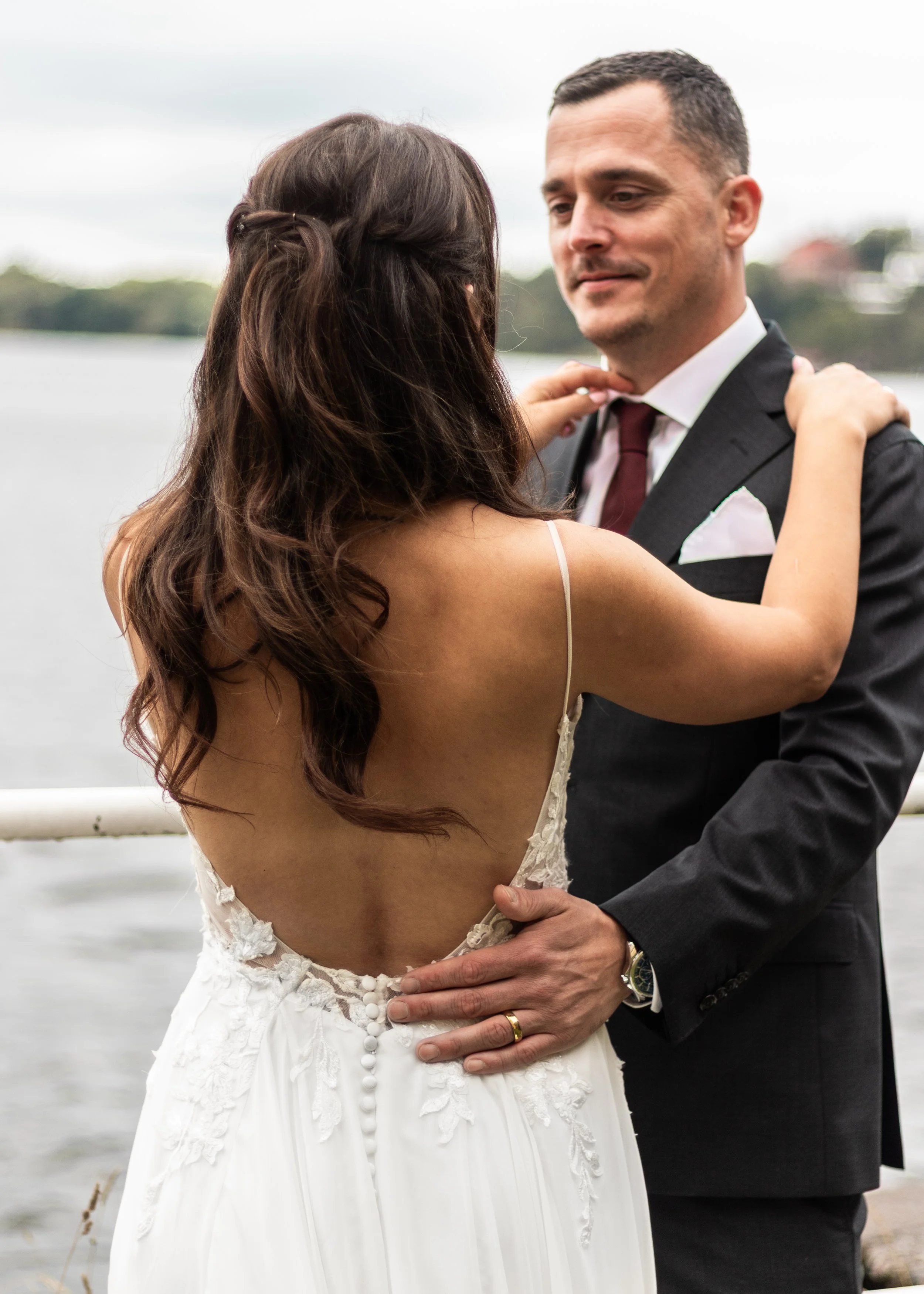 Par på bröllop dansar nära en sjö, kvinna i vit brudklänning och man i svart kostym.