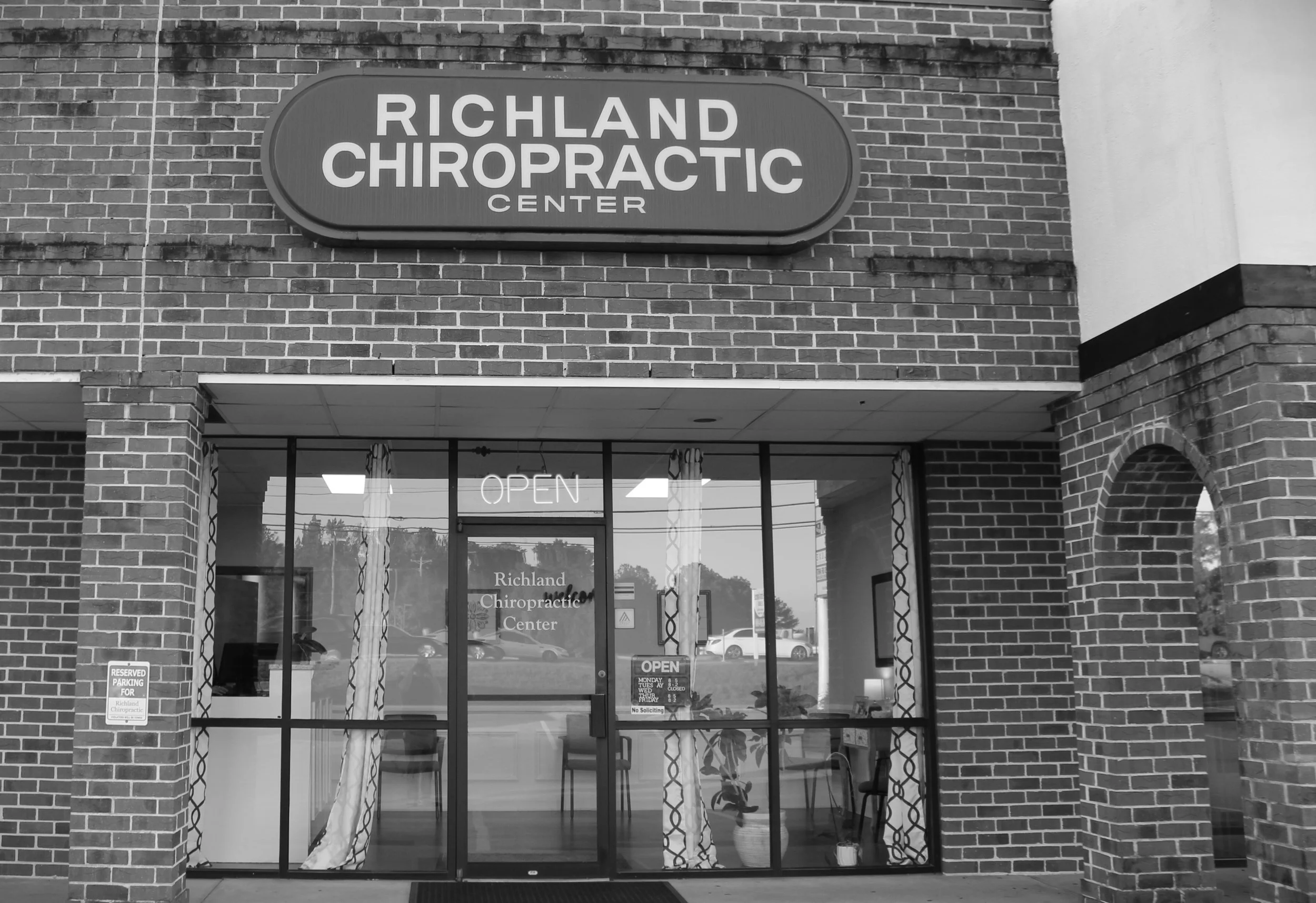 The storefront of Richland Chiropractic Center with a large sign above the entrance, glass doors, and windows, and an illuminated 'OPEN' sign inside.