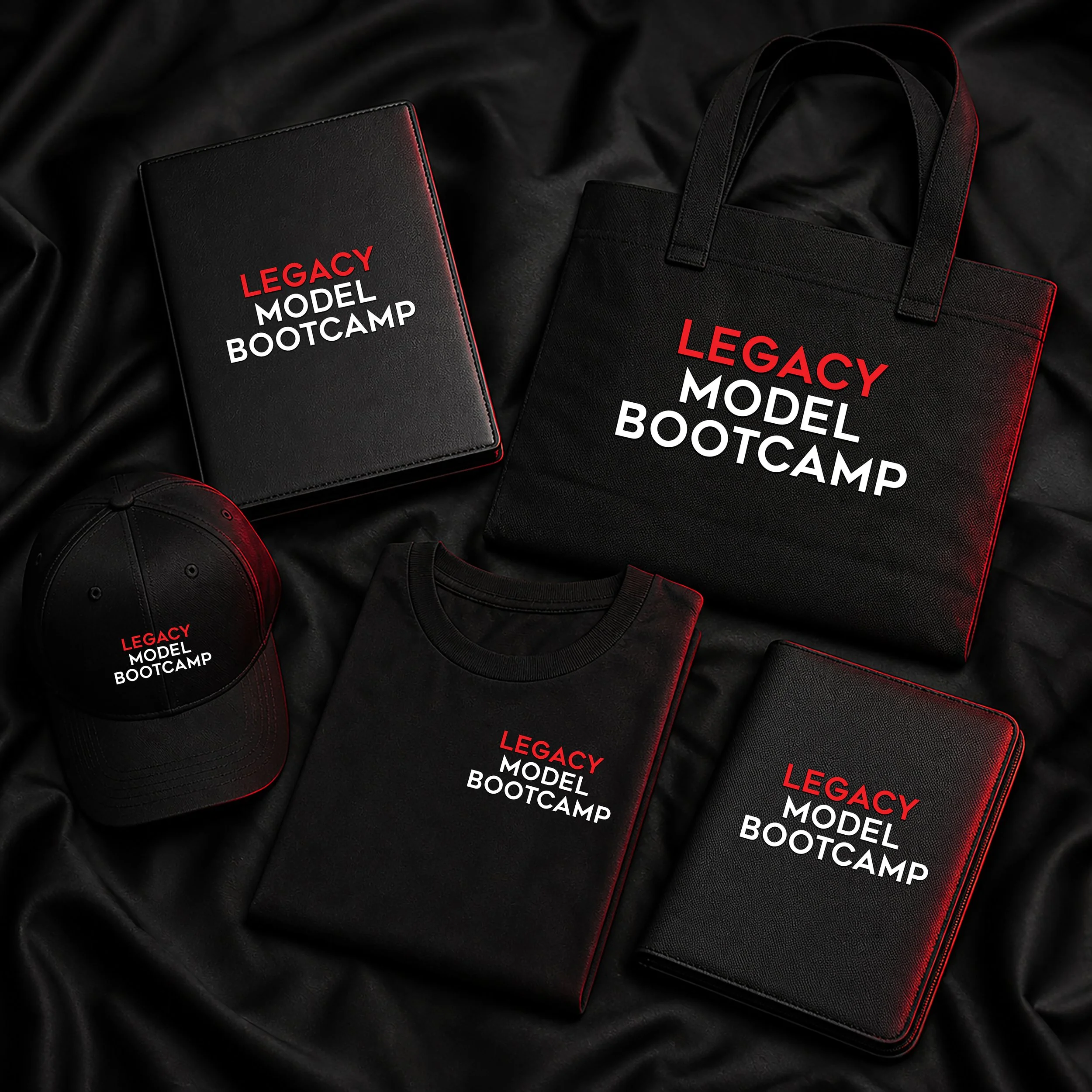 Black notebook, black tote bag, and black cap all with red and white text that reads "LEGACY MODEL BOOTCAMP," placed on black fabric.