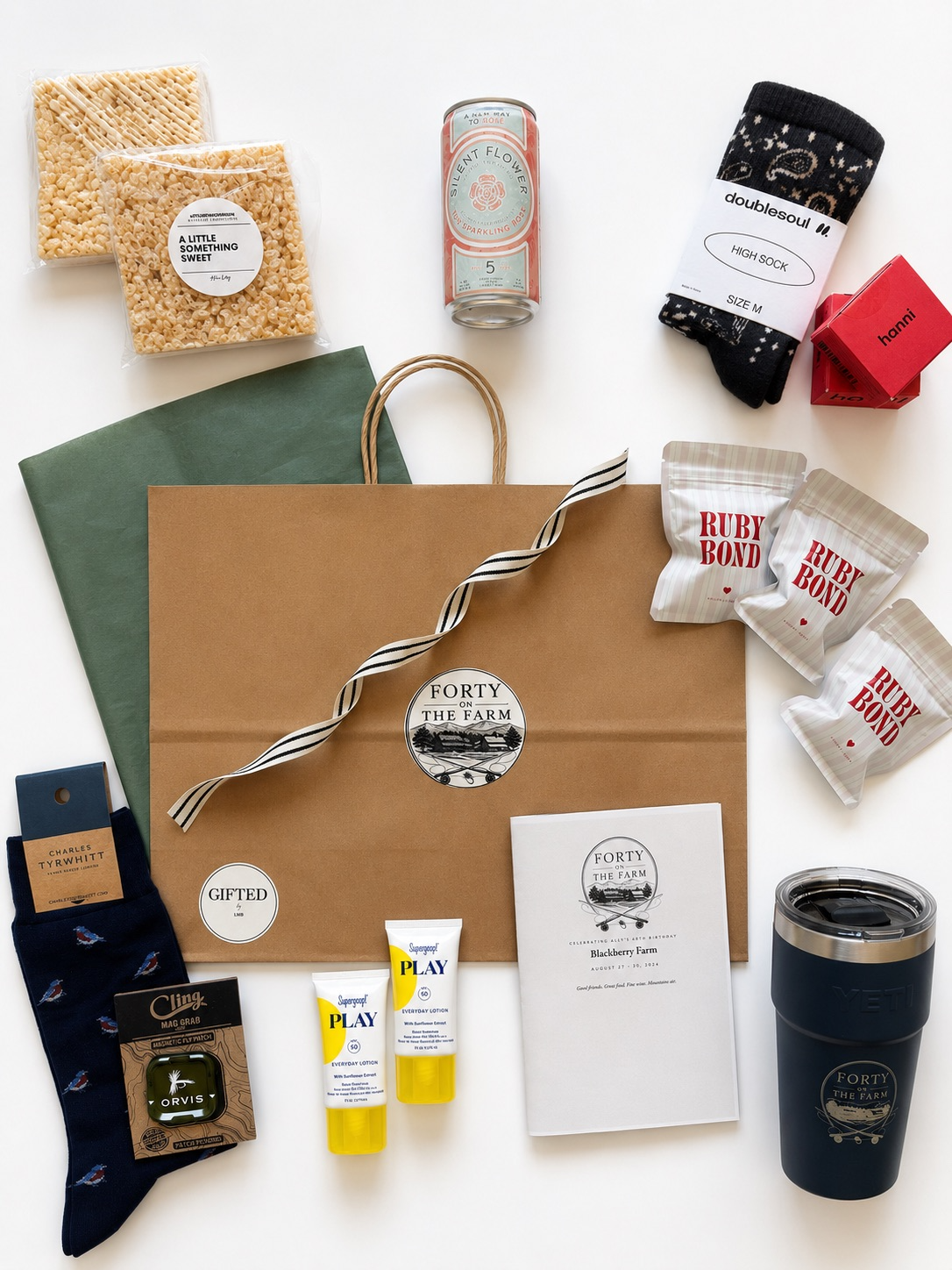 Collection of various items including snacks, beverages, socks, a gift bag, a tumbler, and small gifts on a white surface.