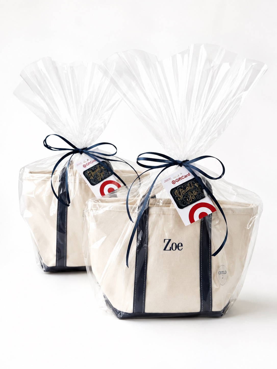 Two gift bags wrapped in clear plastic with black ribbons and tags, one with the name Zoe printed on it.