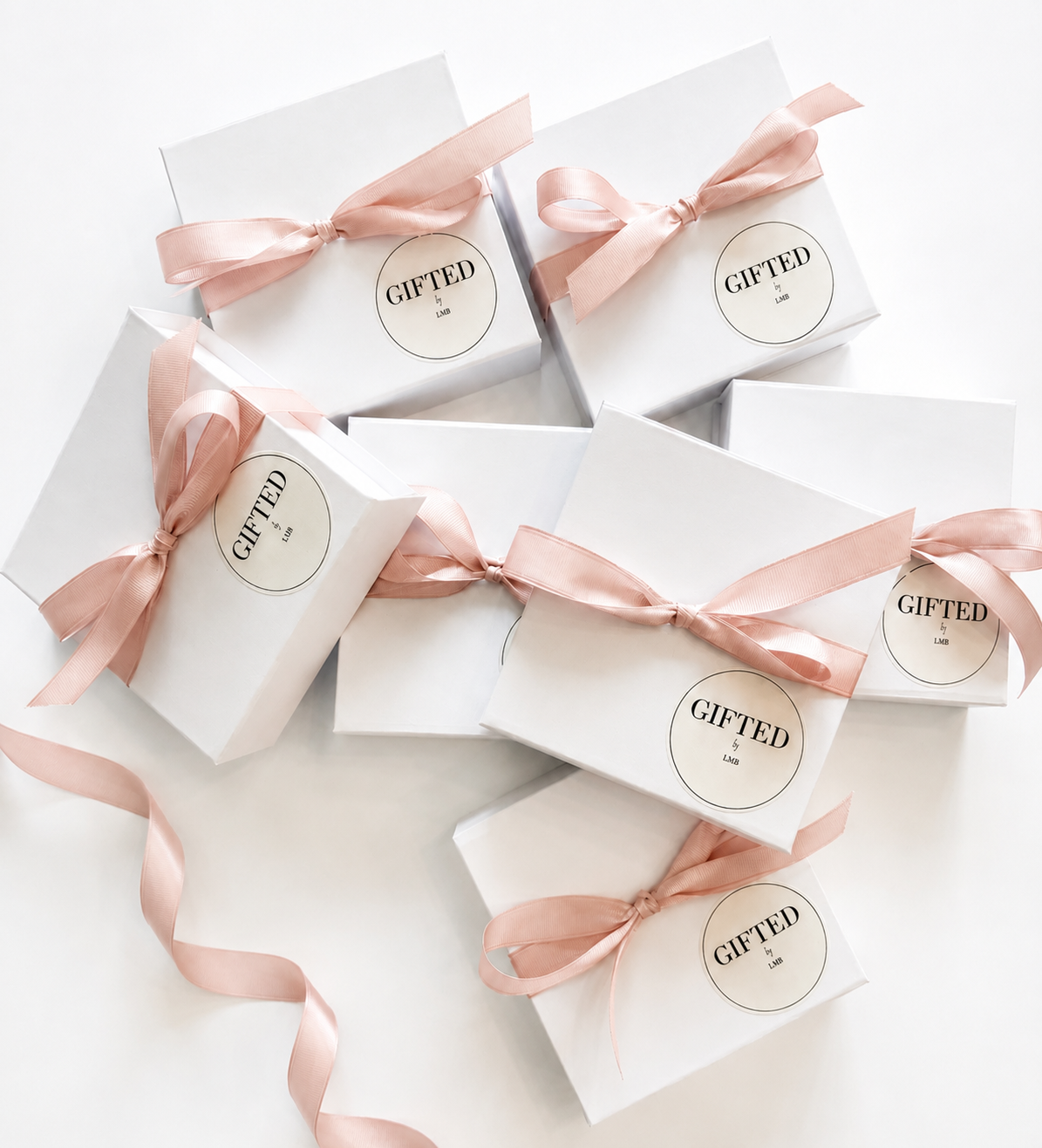 Several white gift boxes decorated with pink ribbons and labels that read 'GIFTED by LMB' scattered on a white surface.