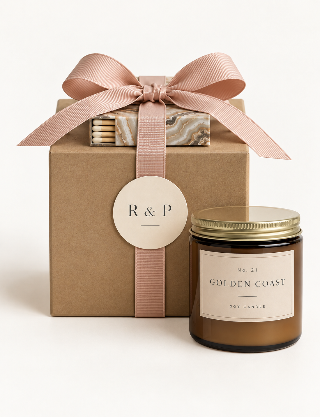A gift box with a pink ribbon and a tag marked 'R & P' is accompanied by a brown soy candle labeled 'Golden Coast' in a glass jar.