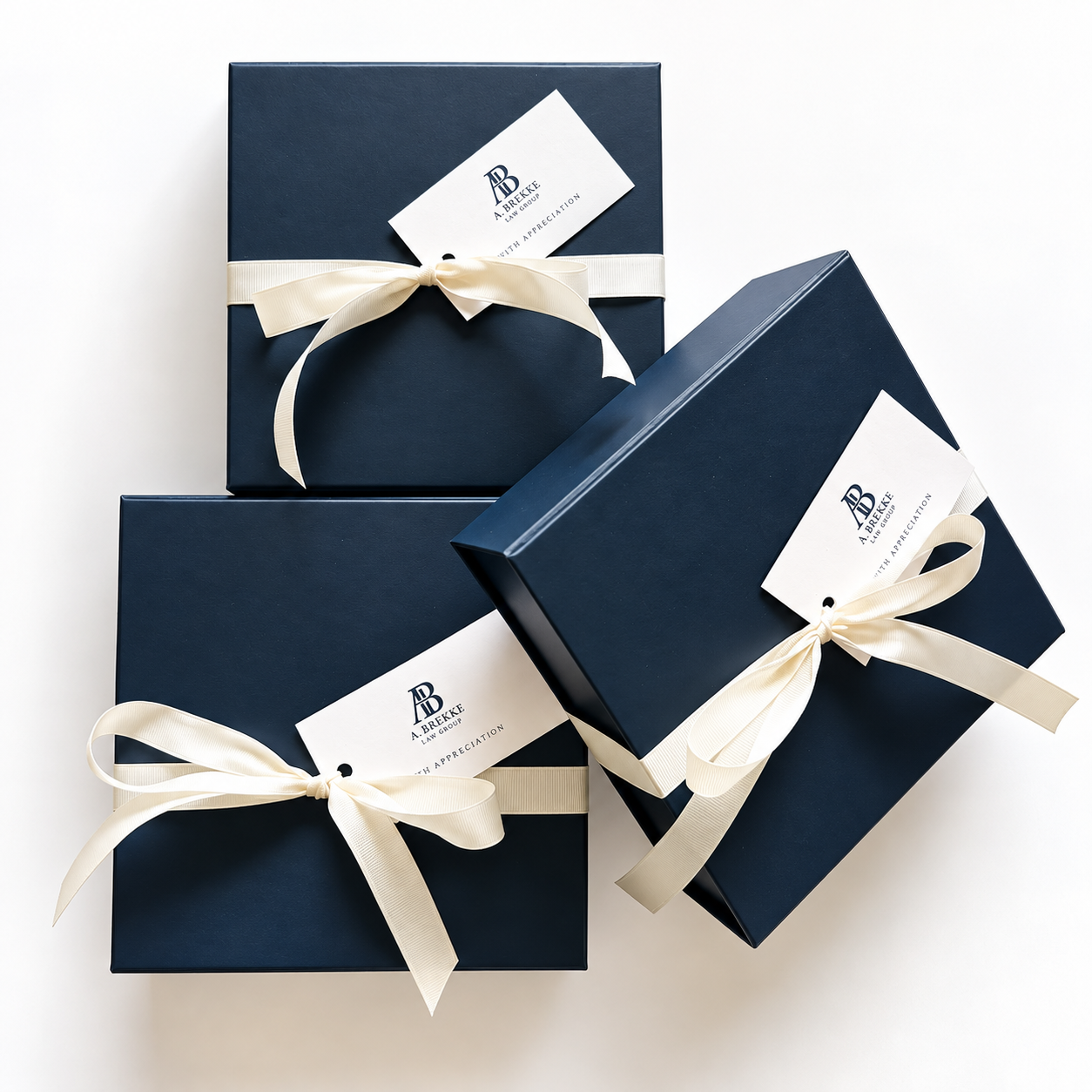 Three navy blue gift boxes tied with cream-colored ribbons, with one box slightly tilted, all on a white background. Each box has a branded label that reads "A. BREUKE LAW GROUP WITH APPRECIATION."