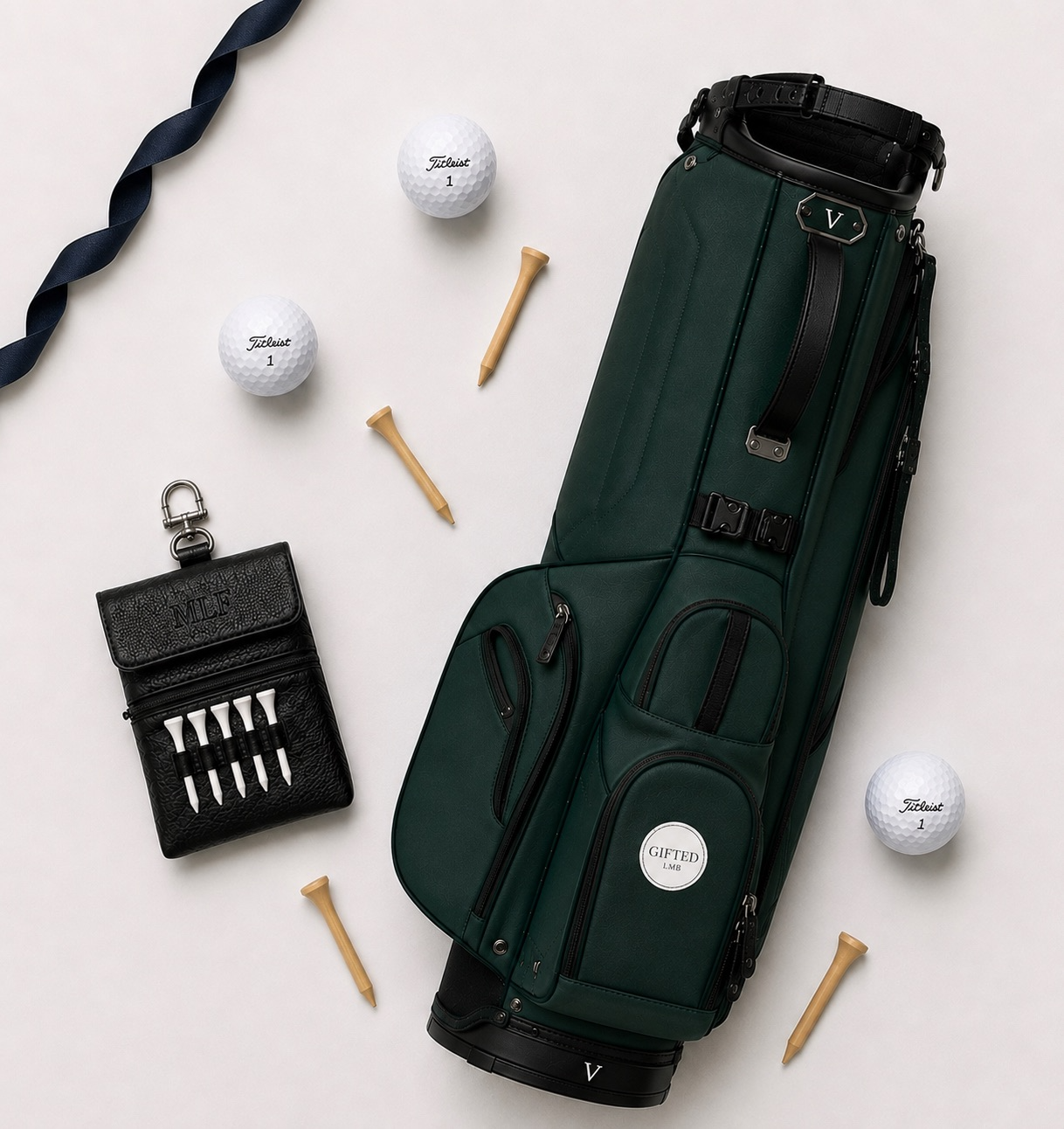 A golf bag with golf clubs, two golf balls labeled 'Titleist 1', a black leather accessory with golf tees, four wooden golf tees, and a navy blue golf towel on a white background.
